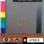 camera app interface displaying settings and color chart digital production Screenshot einer Belichtungsmesser-App, die Informationen wie EV-Werte, Zeit, Blende und ISO anzeigt. Im Hintergrund sind Farbskalen sichtbar.
