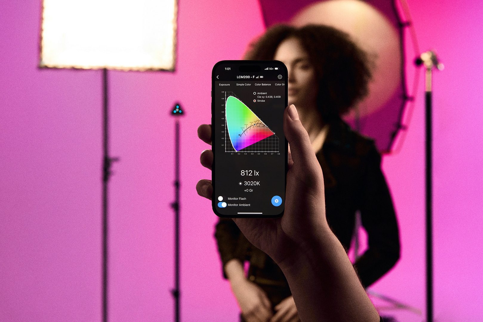 a person holding a smartphone displaying a color spectrum graph in front of a subject with curly hair illuminated by soft pink studio lights digital production A person holding a smartphone displaying a color spectrum graph in front of a subject with curly hair, illuminated by soft pink studio lights.
