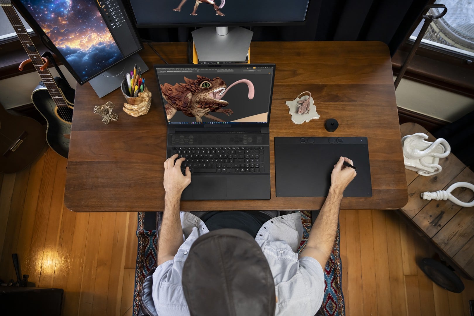 an overhead view of a person sitting at a wooden desk working on a digital art project on a laptop with a stylus surrounded by art supplies and a monitor displaying an intricate creation decor items are partially visible around the workspace digital production An overhead view of a person sitting at a wooden desk, working on a digital art project on a laptop with a stylus, surrounded by art supplies and a monitor displaying an intricate creation. Decor items are partially visible around the workspace.