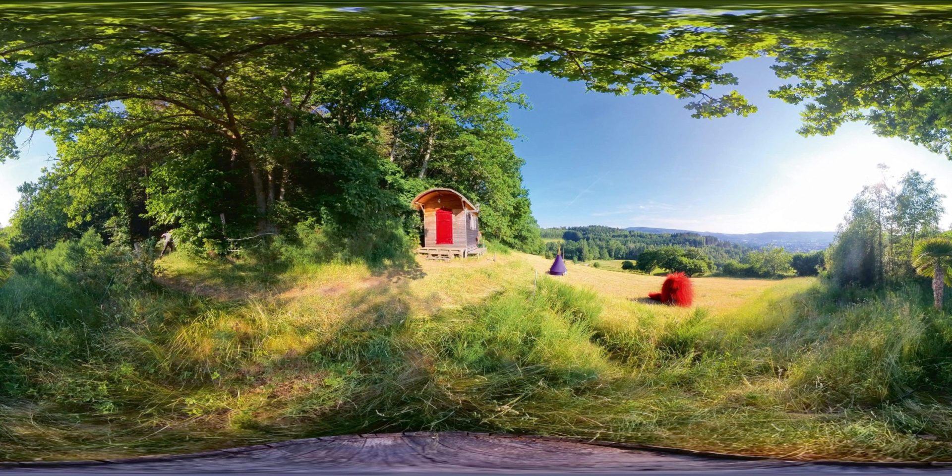 a panoramic view of a rural landscape featuring a small wooden cabin with a red door surrounded by green grass and trees with fields in the background under a clear blue sky digital production A panoramic view of a rural landscape featuring a small wooden cabin with a red door, surrounded by green grass and trees, with fields in the background under a clear blue sky.