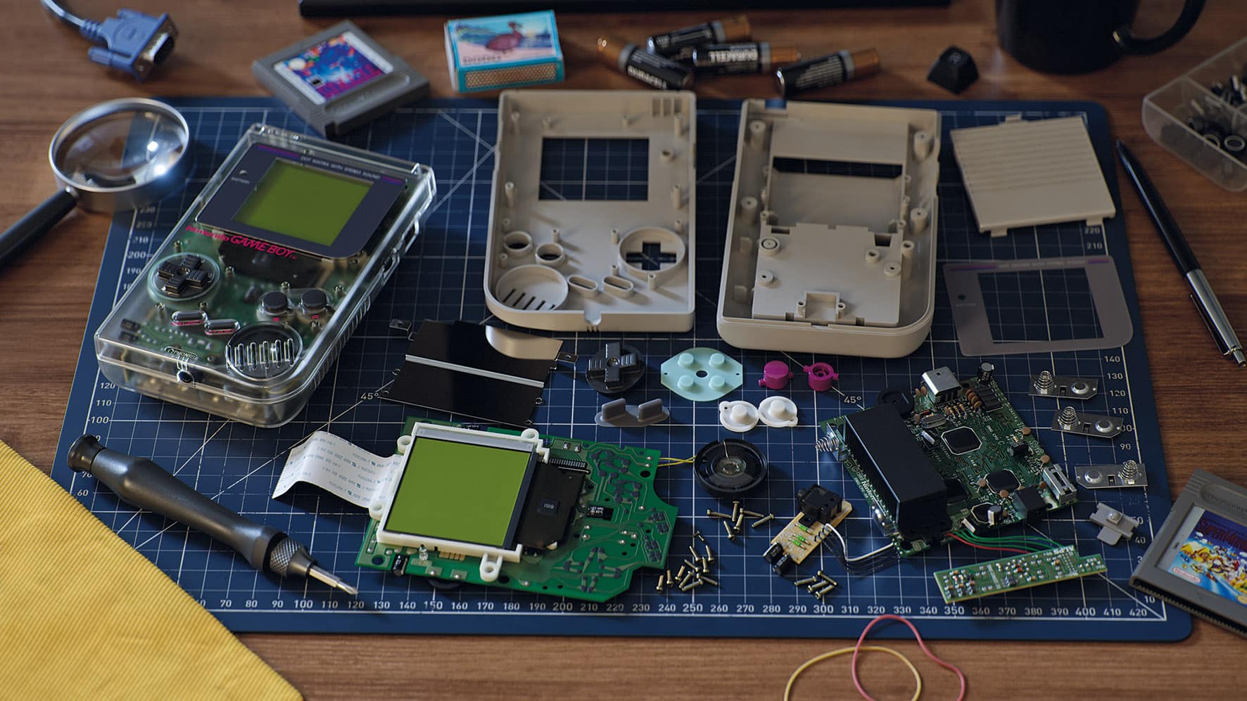 an assortment of disassembled handheld gaming consoles and components laid out on a blue cutting mat tools batteries and game cartridges are also visible in the scene showcasing a repair or modding workspace digital production An assortment of disassembled handheld gaming consoles and components laid out on a blue cutting mat. Tools, batteries, and game cartridges are also visible in the scene, showcasing a repair or modding workspace.