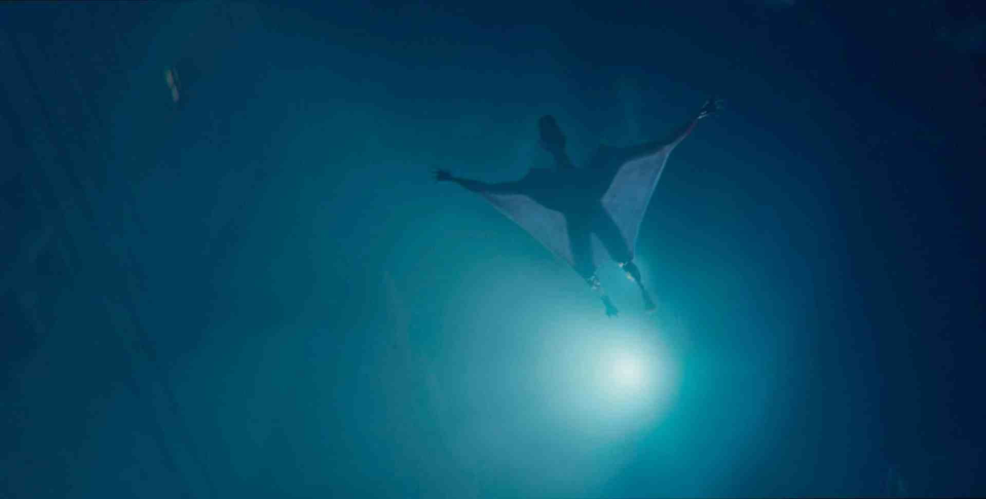 a person in a winged suit gliding through dark waters illuminated by a bright light below the scene captures an underwater environment with an ethereal glow digital production A person in a winged suit gliding through dark waters illuminated by a bright light below. The scene captures an underwater environment with an ethereal glow.