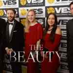 five individuals posing together at a red carpet event for the visual effects society smiling and dressed in formal attire with a backdrop featuring the ves logo and the text the beauty in large font digital production Five individuals posing together at a red carpet event for the Visual Effects Society, smiling and dressed in formal attire, with a backdrop featuring the VES logo and the text 'THE BEAUTY' in large font.