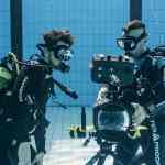 two scuba divers underwater examining underwater filming equipment with a camera visible they are wearing diving suits and accessories surrounded by blue tiled walls of a swimming pool digital production Two scuba divers underwater examining underwater filming equipment, with a camera visible. They are wearing diving suits and accessories, surrounded by blue tiled walls of a swimming pool.