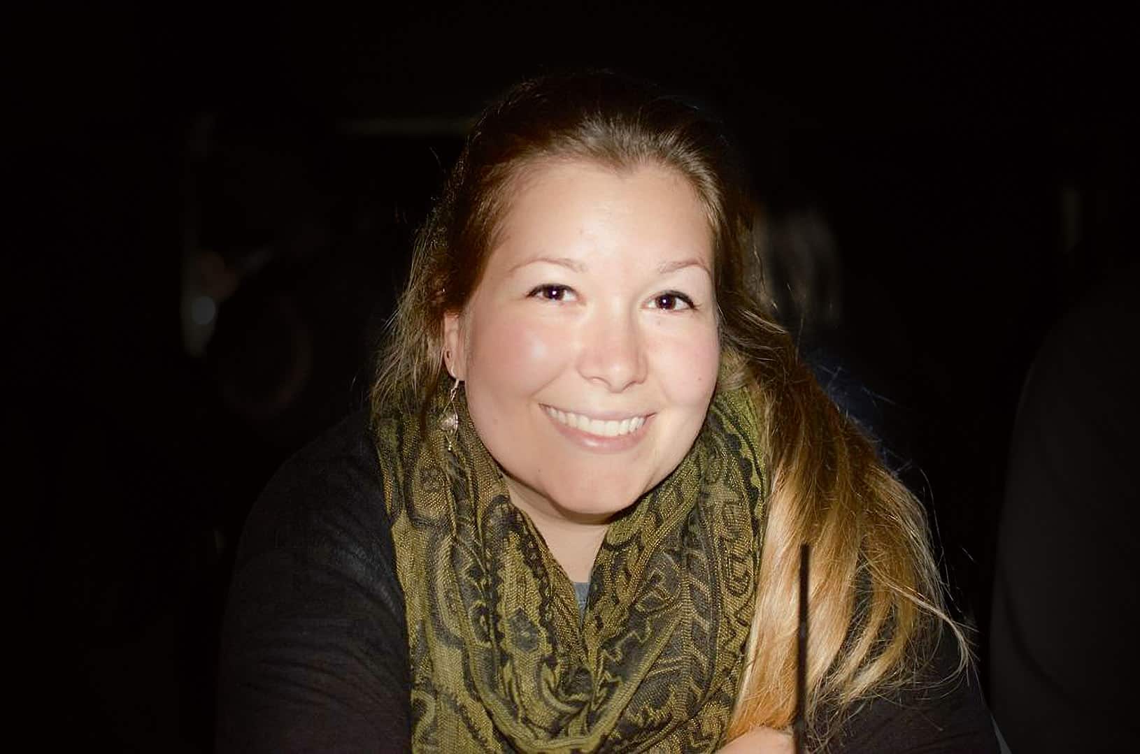 a smiling woman with long hair wearing a patterned scarf in a dimly lit setting digital production A smiling woman with long hair wearing a patterned scarf in a dimly lit setting.
