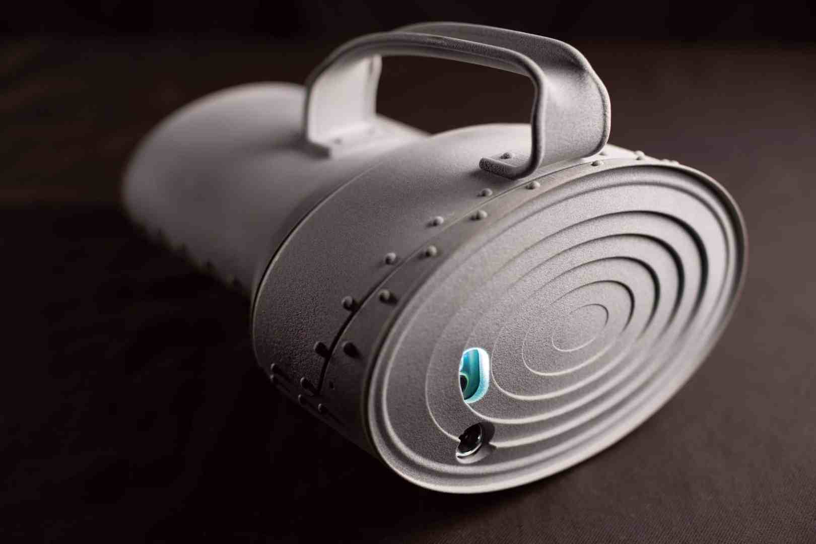 a grey portable speaker with a handle and circular design digital production A grey portable speaker with a handle and circular design.