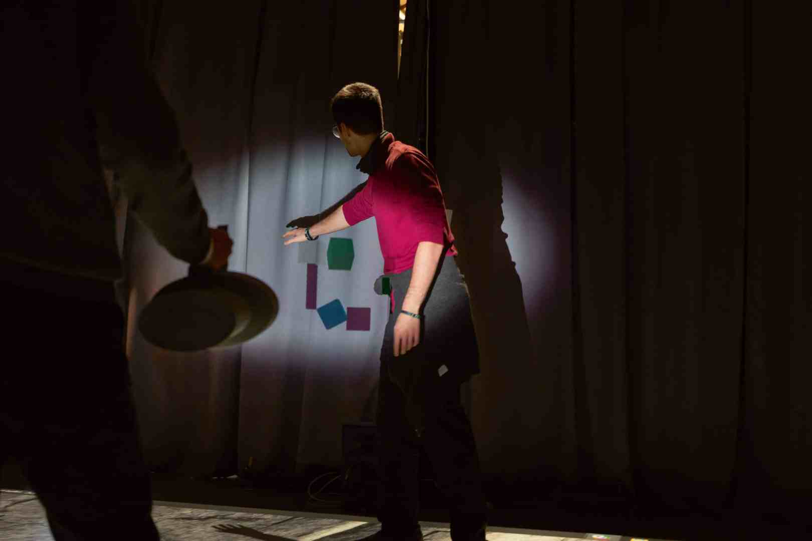 a person gestures towards shapes projected on a curtain digital production A person gestures towards shapes projected on a curtain.