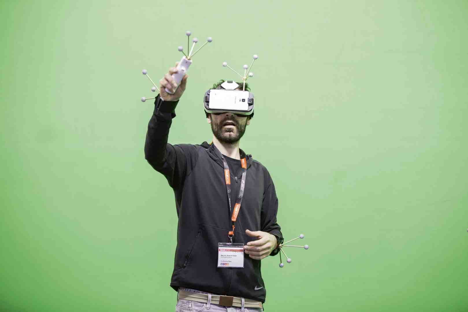 a man wearing a vr headset gesturing with a controller in front of a green screen digital production A man wearing a VR headset gesturing with a controller in front of a green screen.