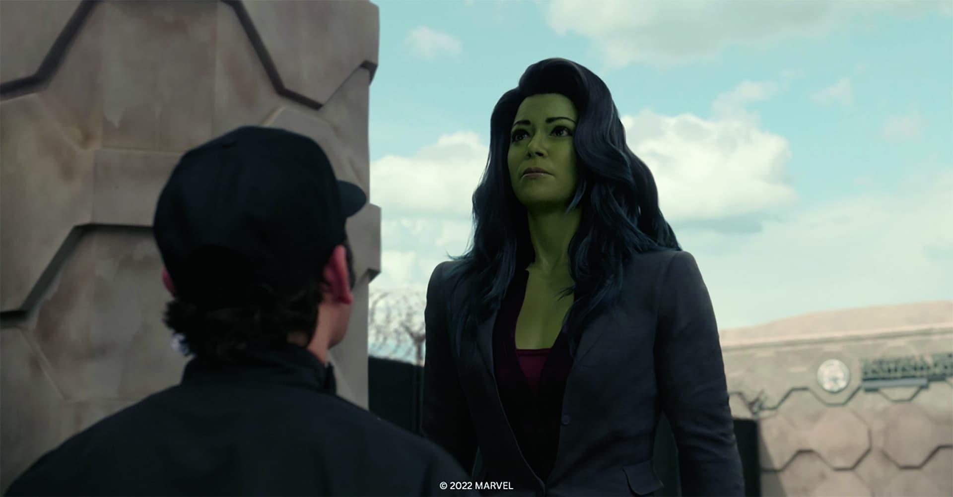 a greenskinned woman in a suit standing before a man in a cap digital production A green-skinned woman in a suit standing before a man in a cap.
