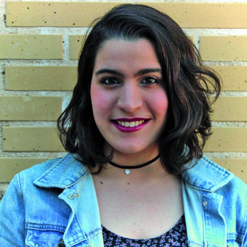 a woman with shoulderlength hair smiling against a brick wall digital production A woman with shoulder-length hair smiling against a brick wall.