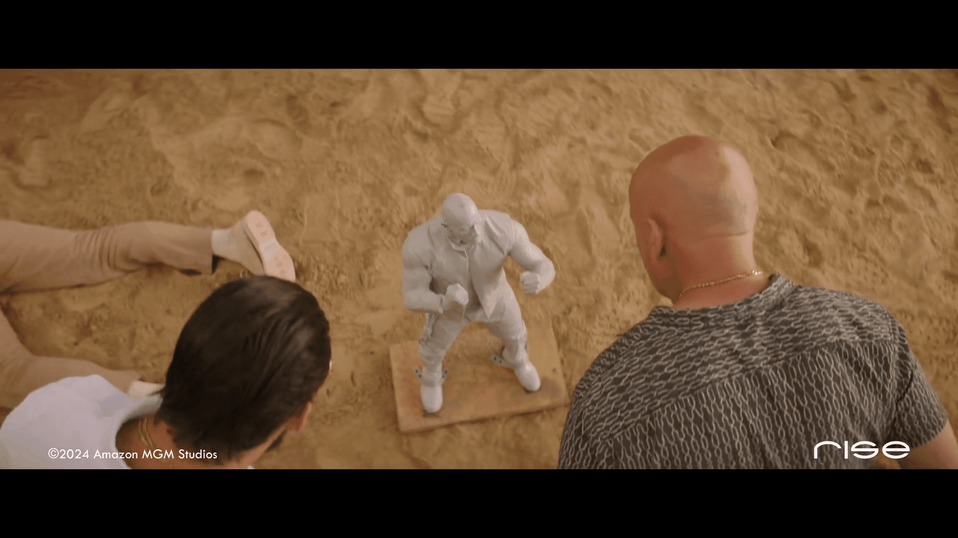 two men observing a white clay sculpture of a muscular figure on sandy ground digital production Two men observing a white clay sculpture of a muscular figure on sandy ground.