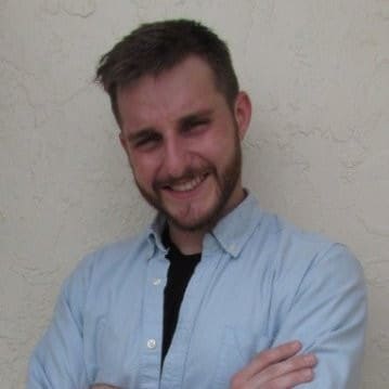 a man smiling confidently with his arms crossed wearing a light blue buttonup shirt over a black shirt against a textured beige wall digital production A man smiling confidently with his arms crossed, wearing a light blue button-up shirt over a black shirt against a textured beige wall.