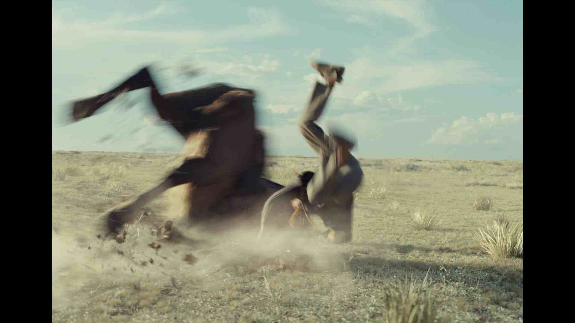 a horse rears up on its hind legs and throws a rider who is falling to the ground in a dry open field under a blue sky dust is kicked up around them as the scene captures movement and tension digital production A horse rears up on its hind legs and throws a rider, who is falling to the ground, in a dry, open field under a blue sky. Dust is kicked up around them as the scene captures movement and tension.