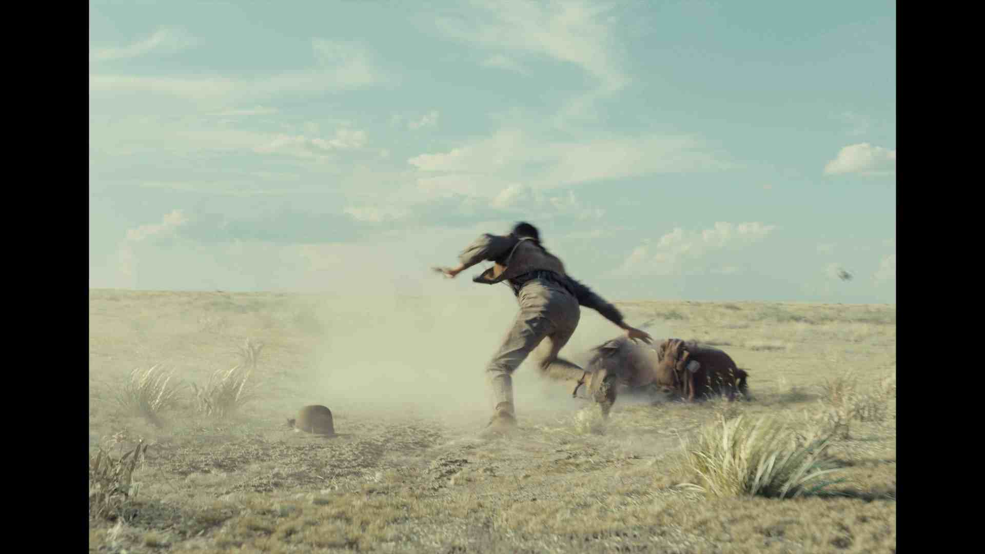 a person running on an open dusty landscape with a blurred motion effect indicating speed the sky is light blue with scattered clouds grass tufts are visible on the ground digital production A person running on an open, dusty landscape, with a blurred motion effect indicating speed. The sky is light blue with scattered clouds. Grass tufts are visible on the ground.