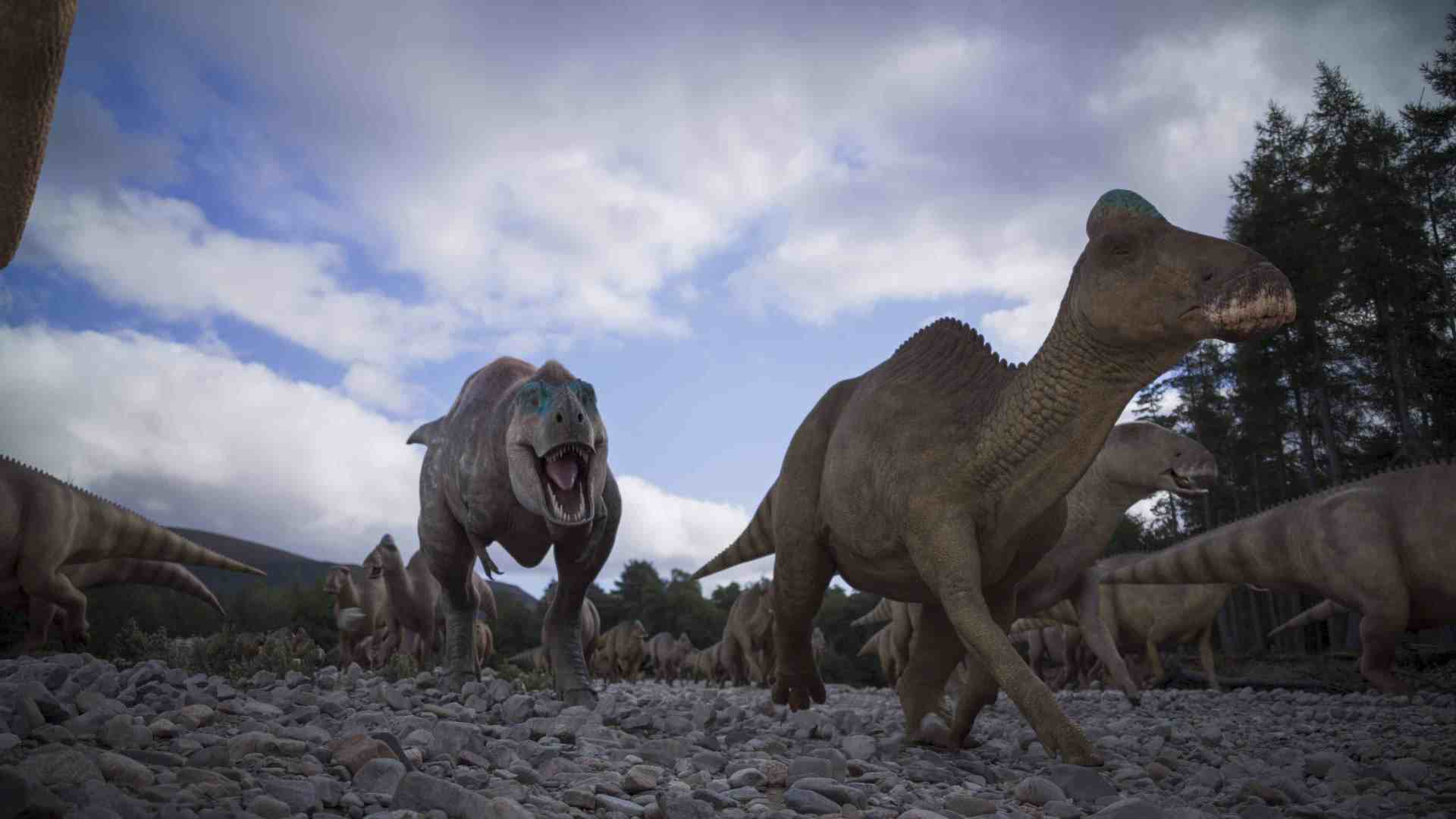 a group of dinosaurs in a rocky landscape under a cloudy sky a large theropod dinosaur with sharp teeth and a fierce expression roars in the foreground while smaller dinosaurs including a hadrosaur roam nearby in a natural setting digital production A group of dinosaurs in a rocky landscape under a cloudy sky. A large theropod dinosaur, with sharp teeth and a fierce expression, roars in the foreground, while smaller dinosaurs, including a hadrosaur, roam nearby in a natural setting.