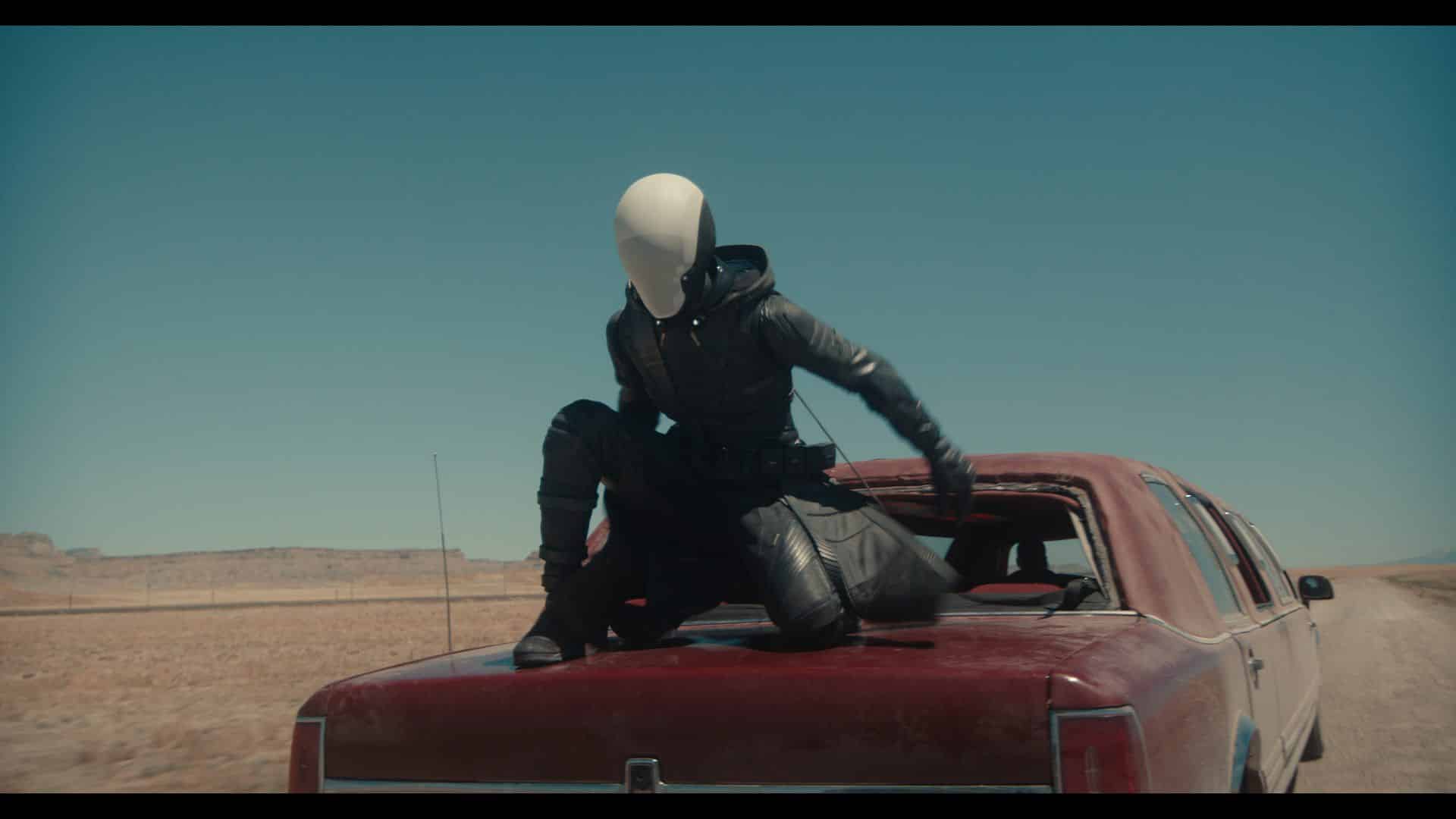 a figure in a dark futuristic outfit and a featureless white mask crouches on the roof of an old red car in a dry barren landscape the expansive sky above is clear emphasizing the desolate surroundings digital production A figure in a dark, futuristic outfit and a featureless white mask crouches on the roof of an old red car in a dry, barren landscape. The expansive sky above is clear, emphasizing the desolate surroundings.
