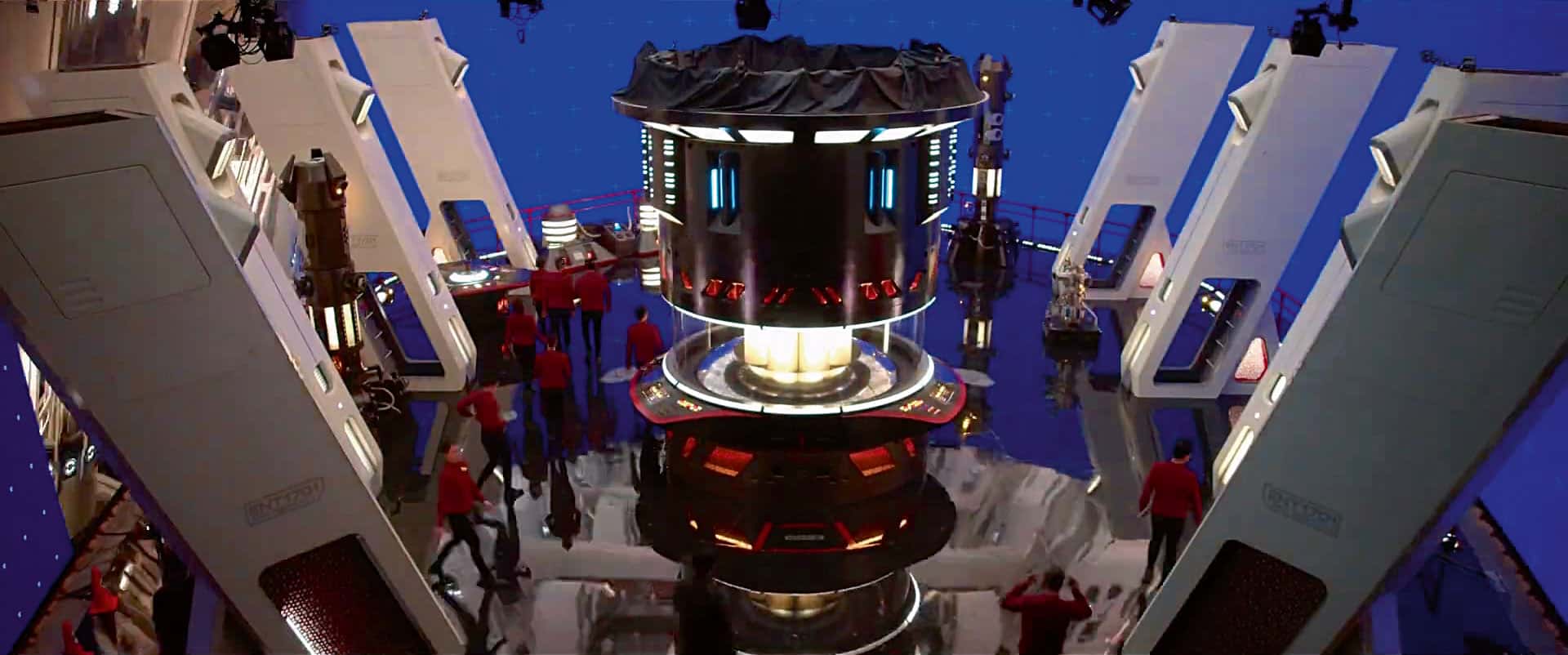 a futuristic control room with sleek white panels and a central console glowing with blue and red lights crew members in red uniforms are engaged in various activities around the hightech setup set against a blue backdrop digital production A futuristic control room with sleek, white panels and a central console glowing with blue and red lights. Crew members in red uniforms are engaged in various activities around the high-tech setup, set against a blue backdrop.