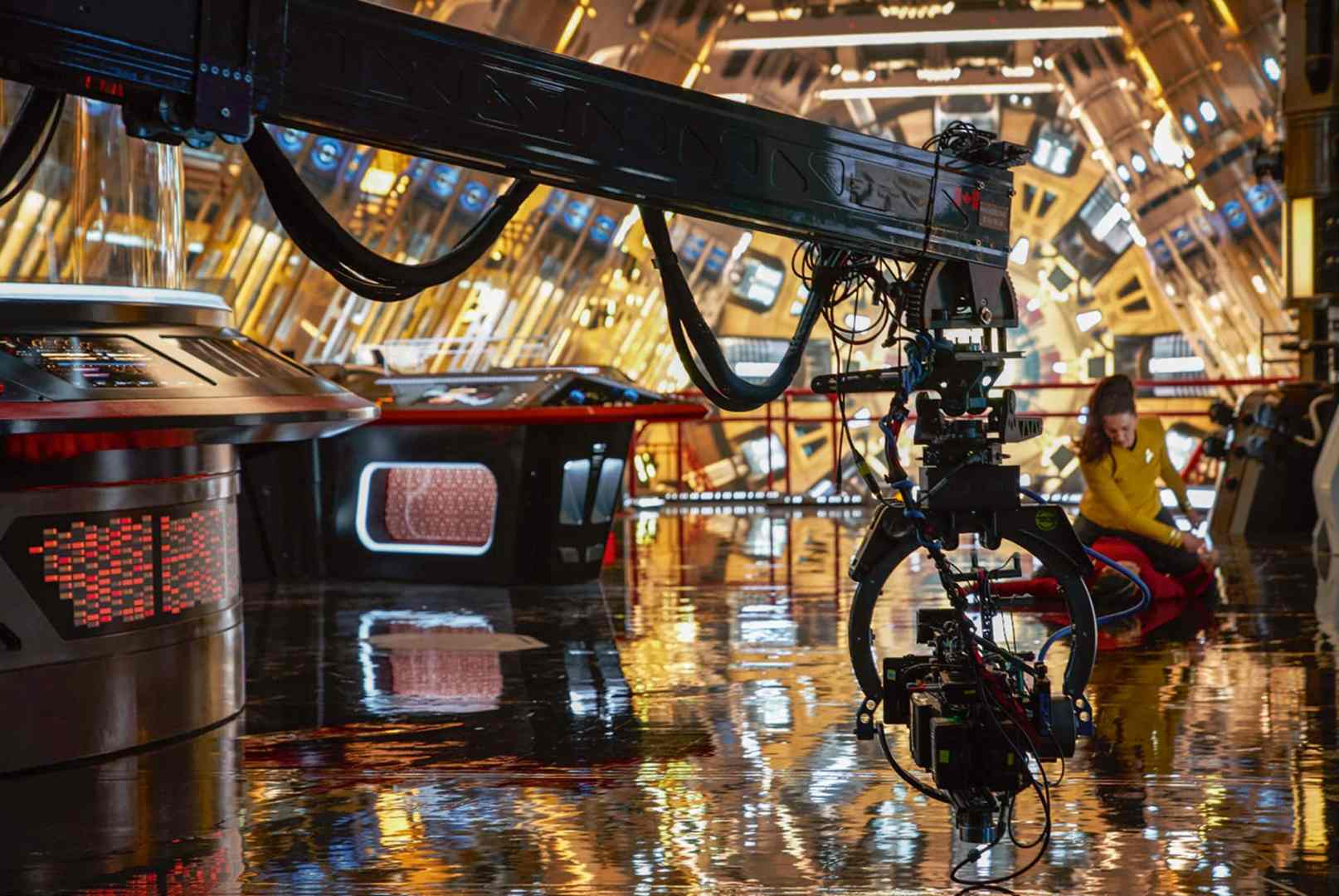 a film set with shiny surfaces reflecting light featuring a large camera crane in the foreground and a child in a yellow outfit playing on the floor the background has futuristic consoles and warm golden lighting digital production A film set with shiny surfaces reflecting light, featuring a large camera crane in the foreground and a child in a yellow outfit playing on the floor. The background has futuristic consoles and warm golden lighting.