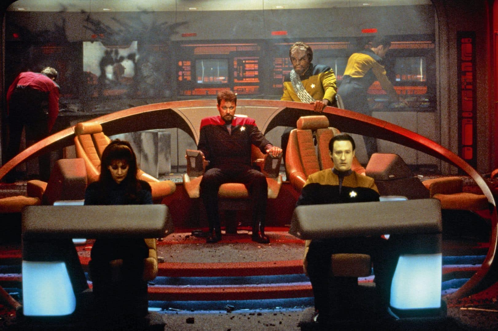 a scene from a starship bridge with five characters a woman in a dark uniform at a console a man in a red uniform seated in the center a man in a yellow uniform standing behind him and a robotic figure beside him all surrounded by control panels in a futuristic setting digital production A scene from a starship bridge with five characters: a woman in a dark uniform at a console, a man in a red uniform seated in the center, a man in a yellow uniform standing behind him, and a robotic figure beside him, all surrounded by control panels in a futuristic setting.