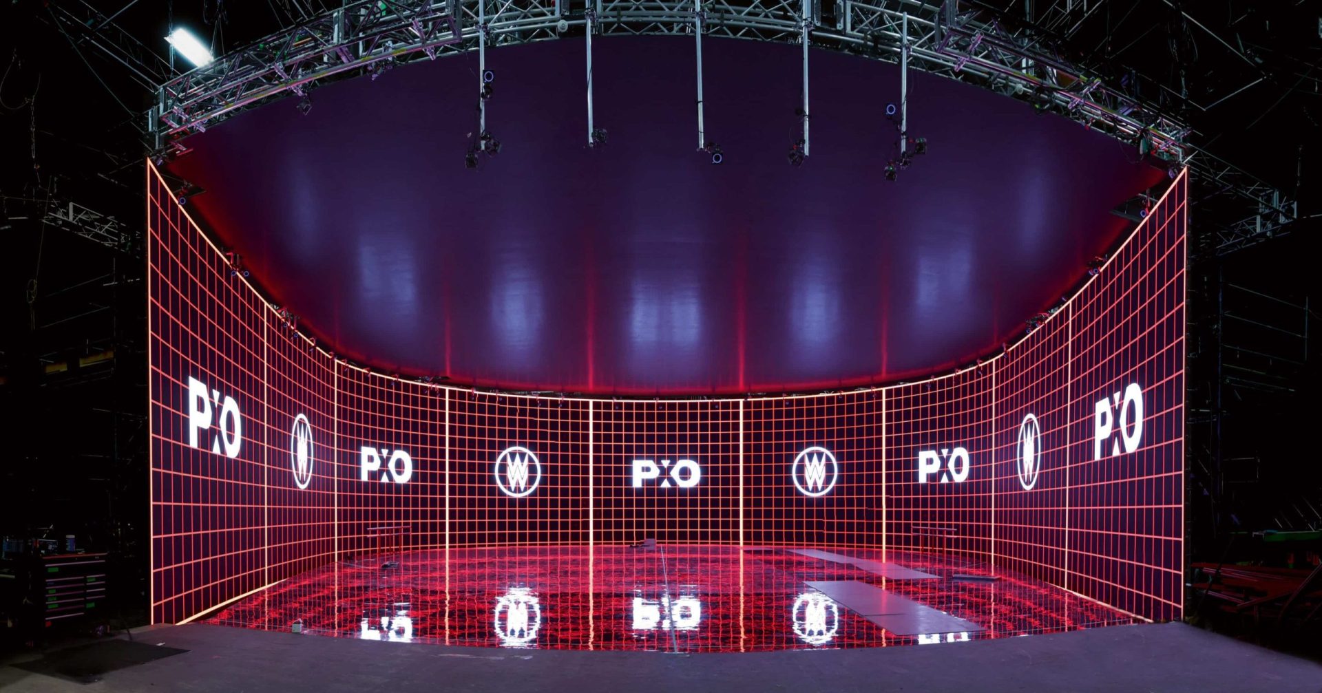 a modern studio space with curved walls illuminated by red grid lighting showcasing the logos po and vw on the walls the ceiling is sleek and reflective emphasizing the futuristic design of the environment digital production A modern studio space with curved walls illuminated by red grid lighting, showcasing the logos 'PO' and 'VW' on the walls. The ceiling is sleek and reflective, emphasizing the futuristic design of the environment.