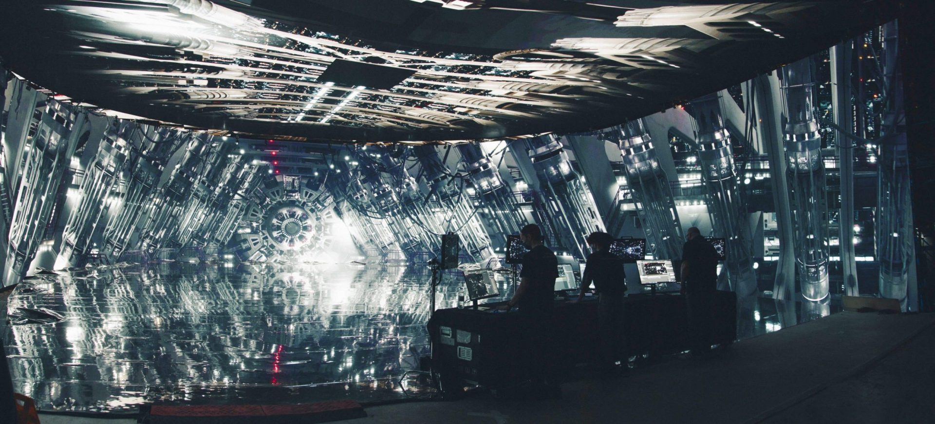 a hightech film set featuring a reflective futuristic interior with mirrored surfaces and intricate lighting several crew members are positioned near production equipment in the foreground contributing to the creative process digital production A high-tech film set featuring a reflective, futuristic interior with mirrored surfaces and intricate lighting. Several crew members are positioned near production equipment in the foreground, contributing to the creative process.