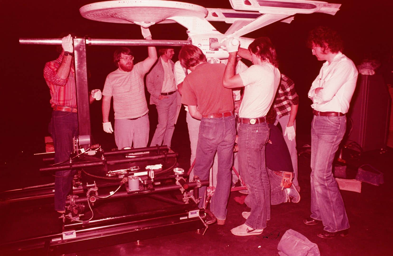 several technicians working together to assemble a model spaceship on a dark stage the group includes men and women some wearing gloves as they focus on the structure above them and adjust various components digital production Several technicians working together to assemble a model spaceship on a dark stage. The group includes men and women, some wearing gloves, as they focus on the structure above them and adjust various components.