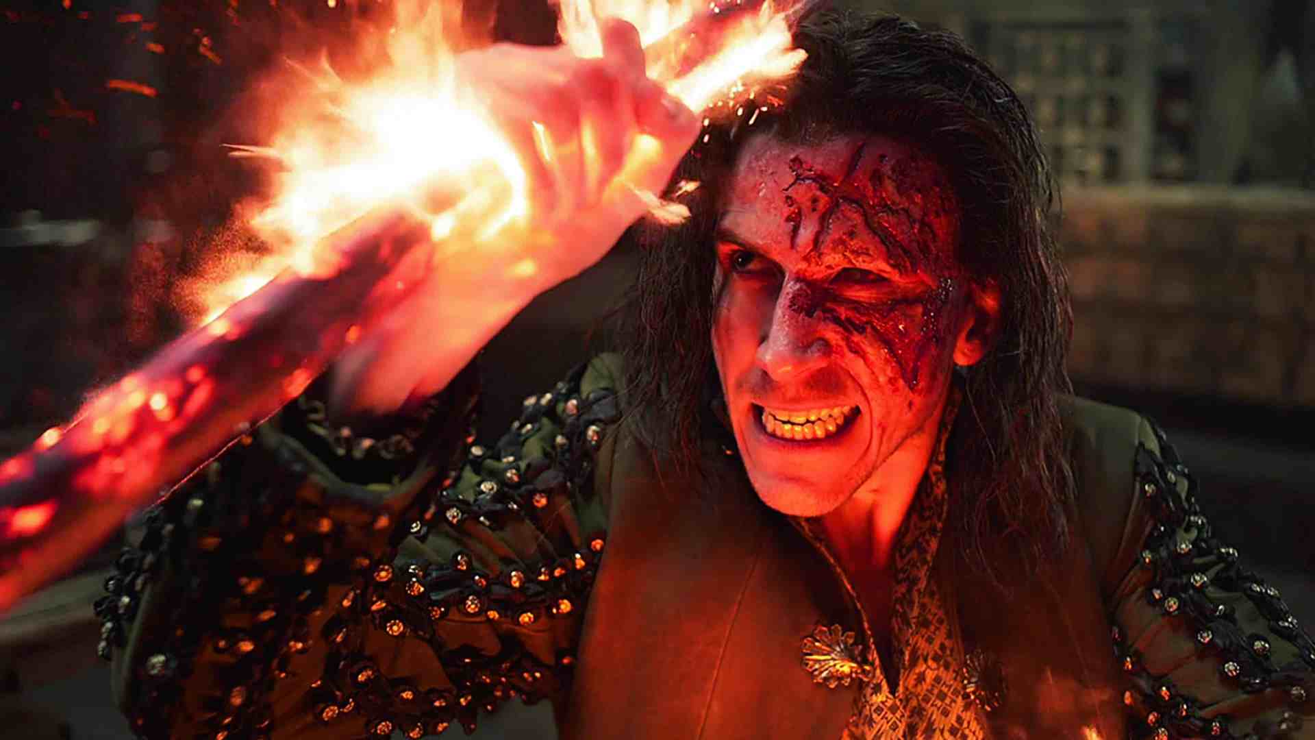 a person with long dark hair wearing a spiked jacket is wielding a flaming staff in a dramatic pose their face shows intense emotion with visible scars and a fierce expression set against a dark atmospheric background digital production A person with long dark hair, wearing a spiked jacket, is wielding a flaming staff in a dramatic pose. Their face shows intense emotion with visible scars and a fierce expression, set against a dark, atmospheric background.