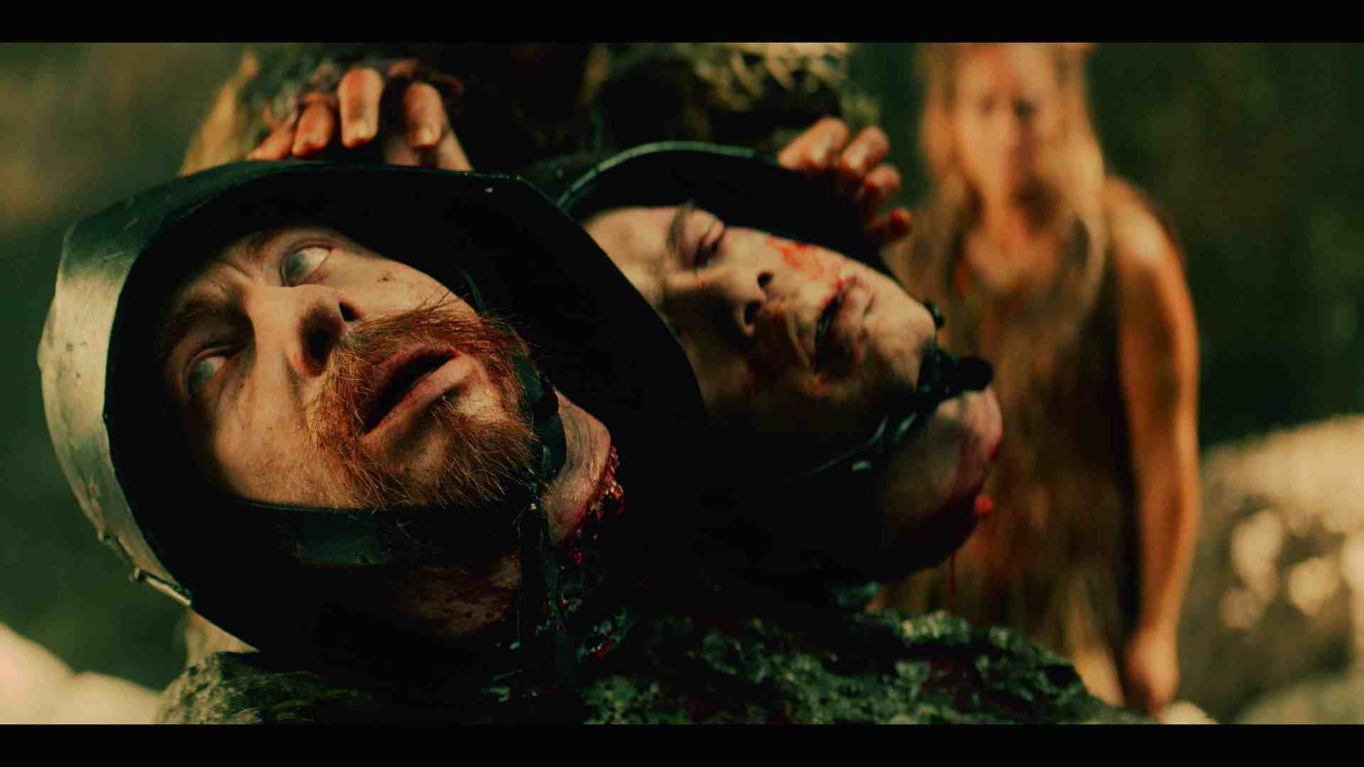 a closeup of two severed heads with blood visible one wearing a helmet while a blurred figure stands in the background the scene has a dark dramatic tone digital production A close-up of two severed heads with blood visible, one wearing a helmet, while a blurred figure stands in the background. The scene has a dark, dramatic tone.