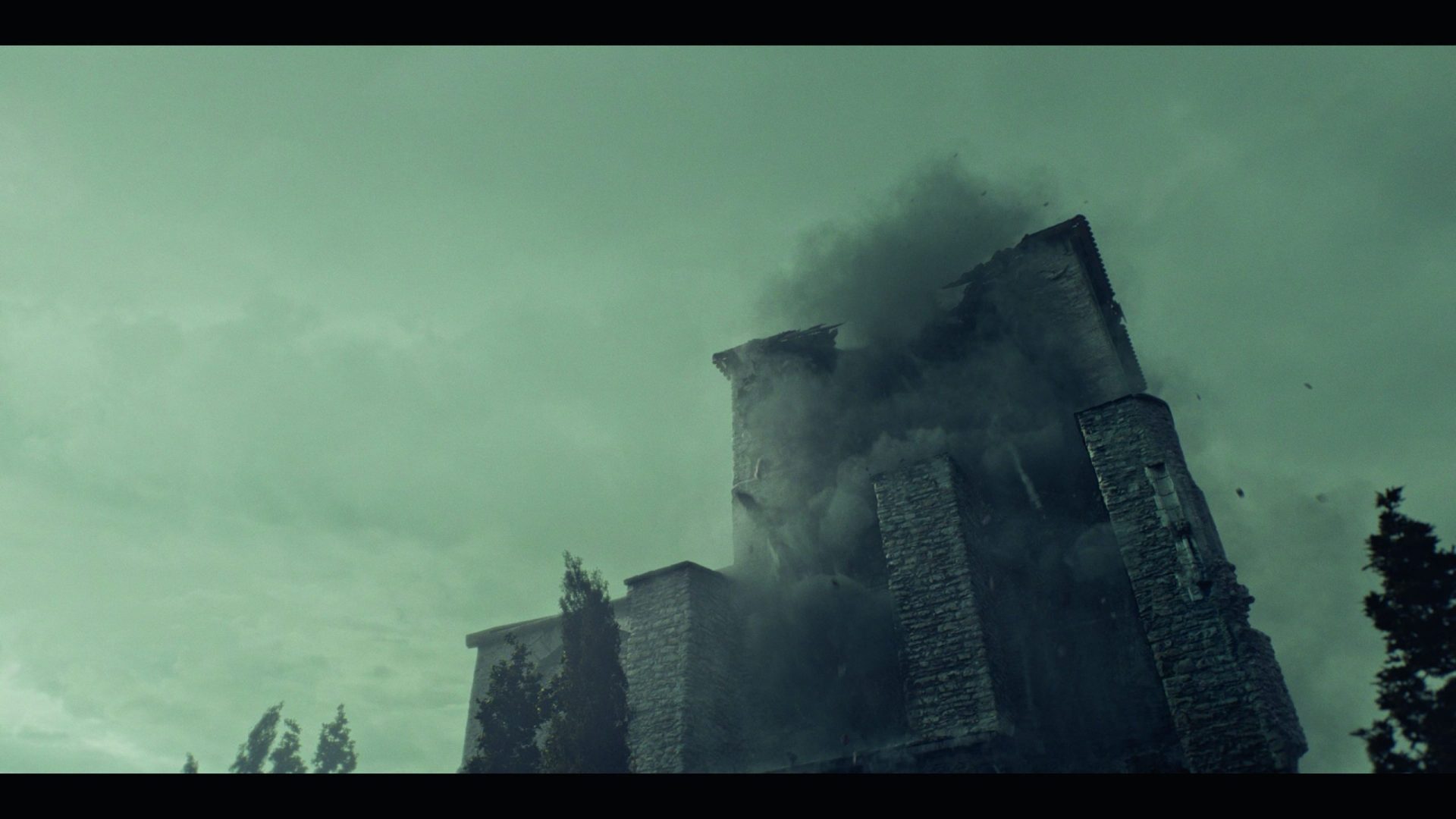 a partially collapsed stone building with smoke billowing from the top set against a cloudy sky trees are visible in the foreground and the scene has a muted color palette digital production A partially collapsed stone building with smoke billowing from the top, set against a cloudy sky. Trees are visible in the foreground, and the scene has a muted color palette.