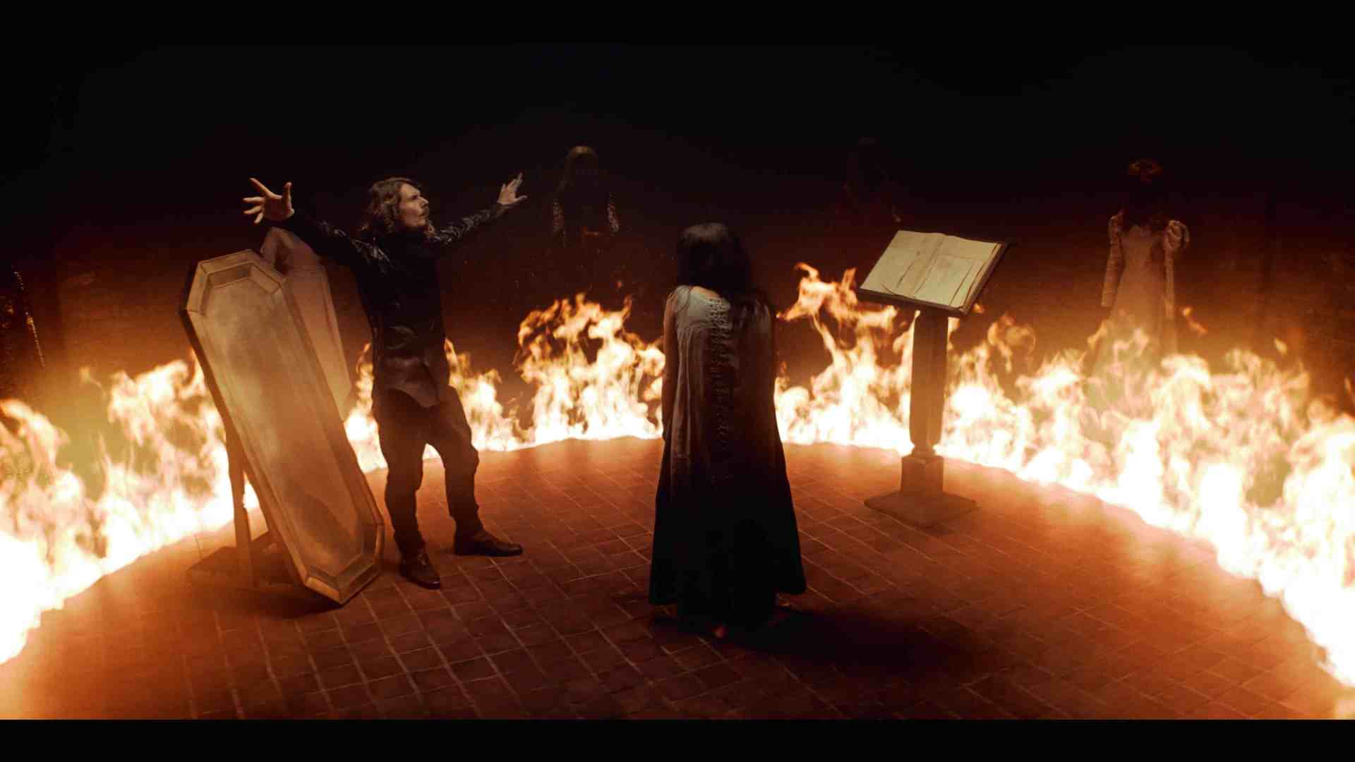 a dramatic scene featuring a man with long hair gesturing dramatically in front of a burning circle while a woman in a dark cloak faces him a wooden podium with an open book stands nearby surrounded by shadowy figures in the background digital production A dramatic scene featuring a man with long hair gesturing dramatically in front of a burning circle, while a woman in a dark cloak faces him. A wooden podium with an open book stands nearby, surrounded by shadowy figures in the background.