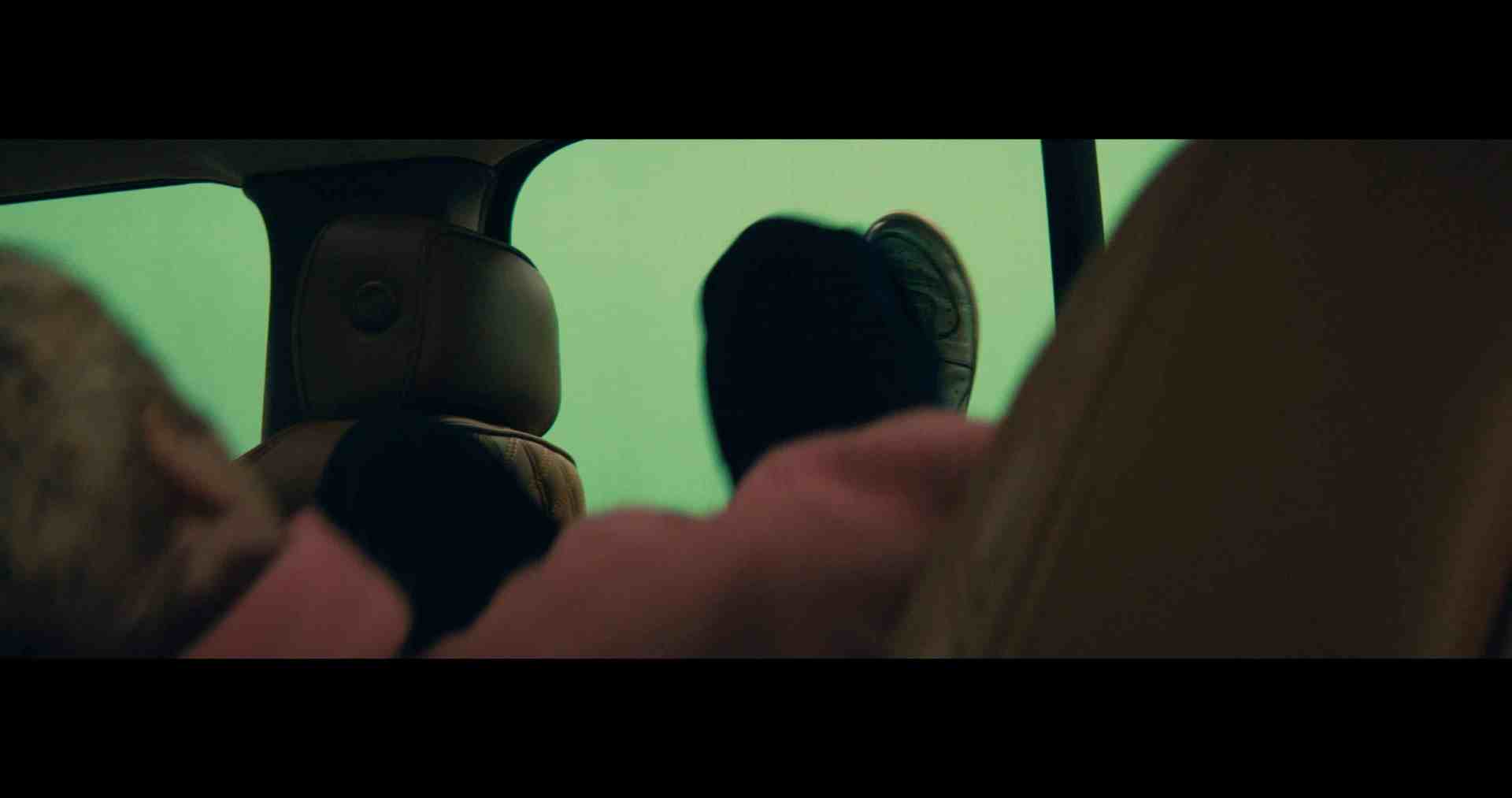 the interior of a vehicle with two partially visible passengers one passenger has short hair and is wearing a pink sweater while the other has a foot resting on the headrest wearing a black shoe the background shows a greenish hue digital production The interior of a vehicle with two partially visible passengers. One passenger has short hair and is wearing a pink sweater, while the other has a foot resting on the headrest, wearing a black shoe. The background shows a greenish hue.