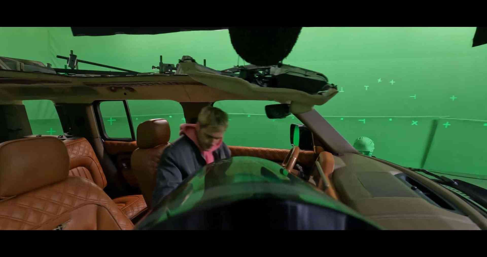 a person in a pink hoodie is seated in the drivers seat of a vehicle with brown leather interior the background features green screen elements indicating a film production setup digital production A person in a pink hoodie is seated in the driver's seat of a vehicle with brown leather interior. The background features green screen elements indicating a film production setup.