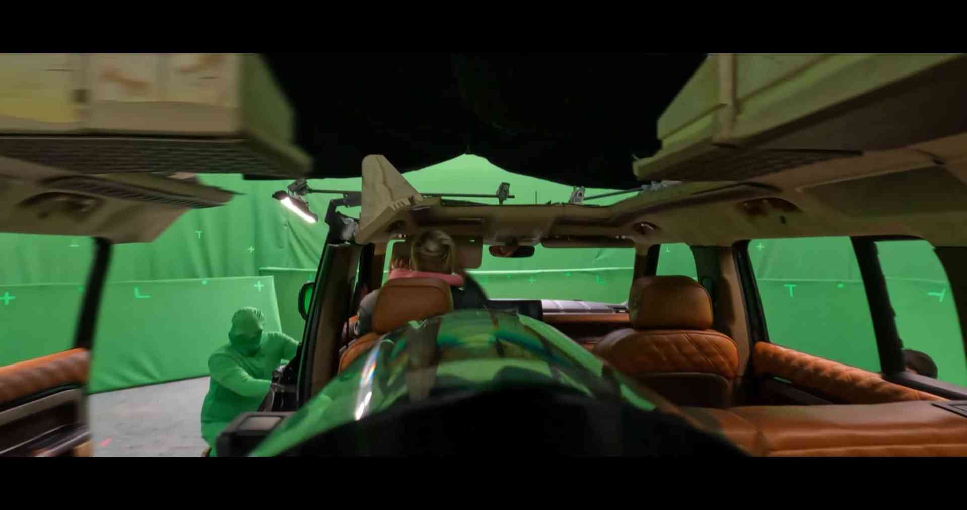 interior view of a vehicle on a film set featuring a green screen backdrop the front seats are plush tan leather with a visible dashboard a crew member in a green suit is adjusting equipment nearby digital production Interior shot of a vehicle during filming, featuring green screens all around, with crew members in the background preparing for a scene.