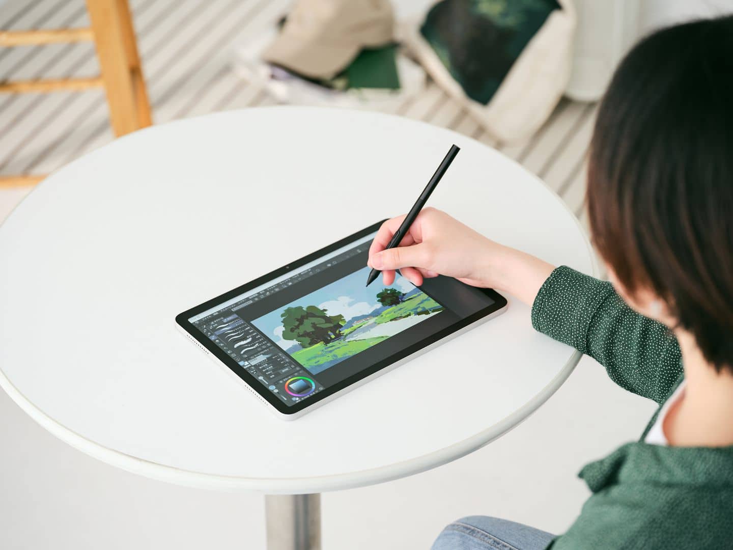 a person with short hair using a digital tablet to draw a landscape scene featuring a tree the tablet is placed on a round white table in a bright modern workspace digital production A person with short hair using a digital tablet to draw a landscape scene featuring a tree. The tablet is placed on a round white table in a bright, modern workspace.