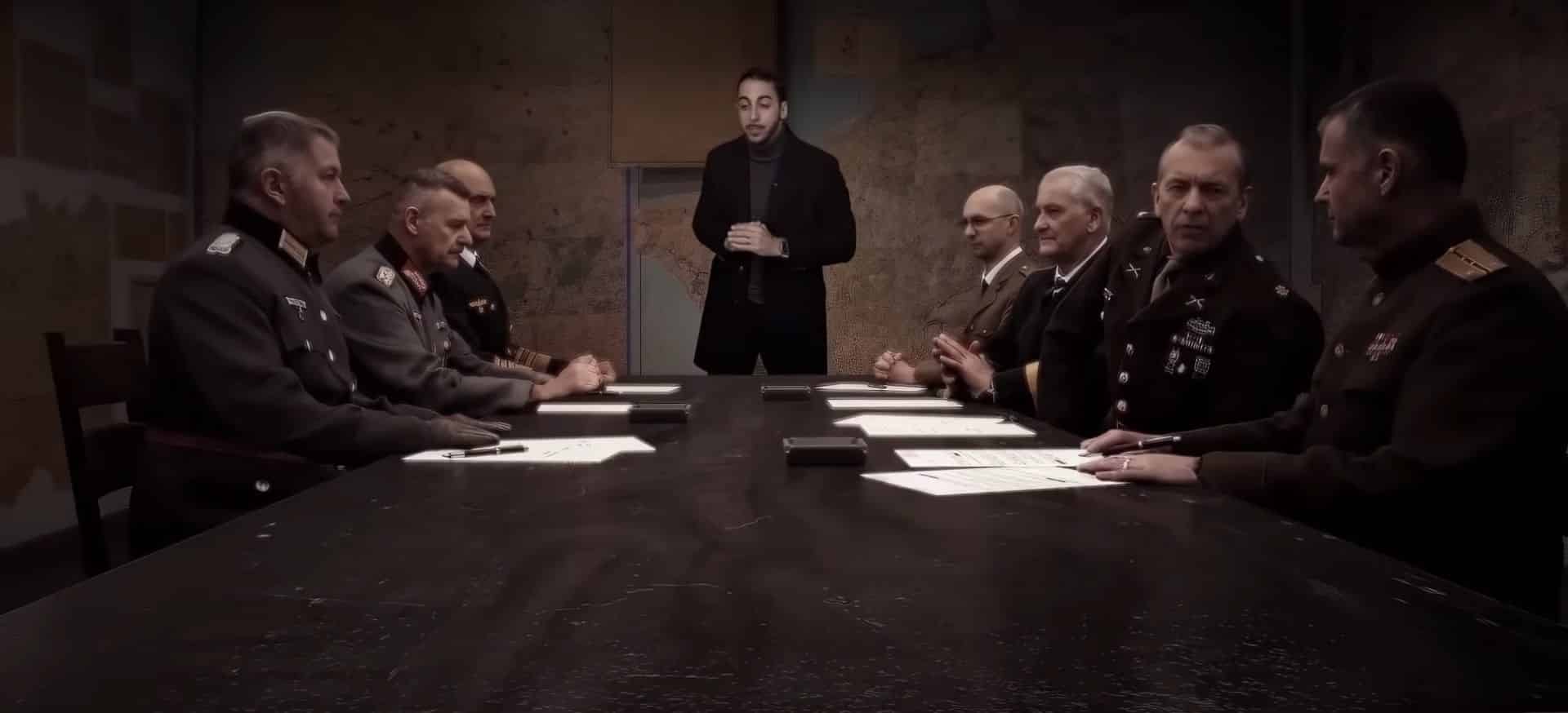 a group of military leaders seated at a long table in a dimly lit room with a standing figure in the center papers and a small black object are visible on the table and maps can be seen on the walls digital production A group of military leaders seated at a long table in a dimly lit room, with a standing figure in the center. Papers and a small black object are visible on the table, and maps can be seen on the walls.