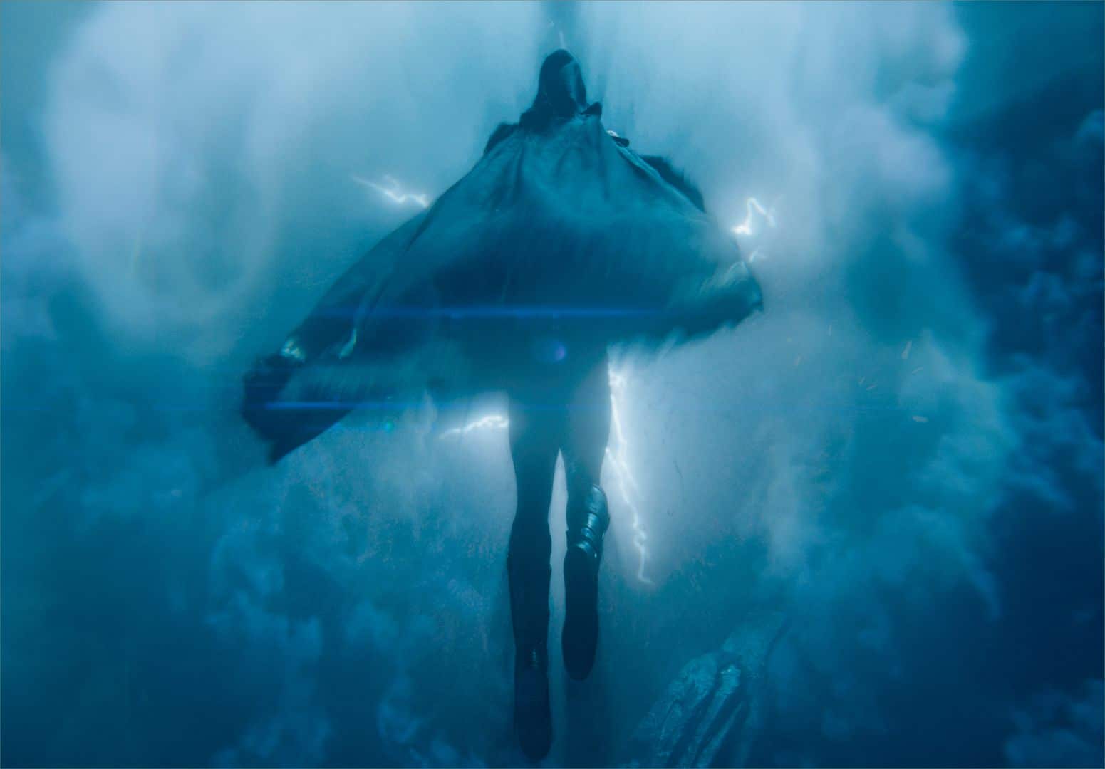 a figure in a dark cape surrounded by swirling blue mist and flashes of light depicted from below the background shows foggy elements and light effects resembling lightning digital production A figure in a dark cape surrounded by swirling blue mist and flashes of light, depicted from below. The background shows foggy elements and light effects resembling lightning.