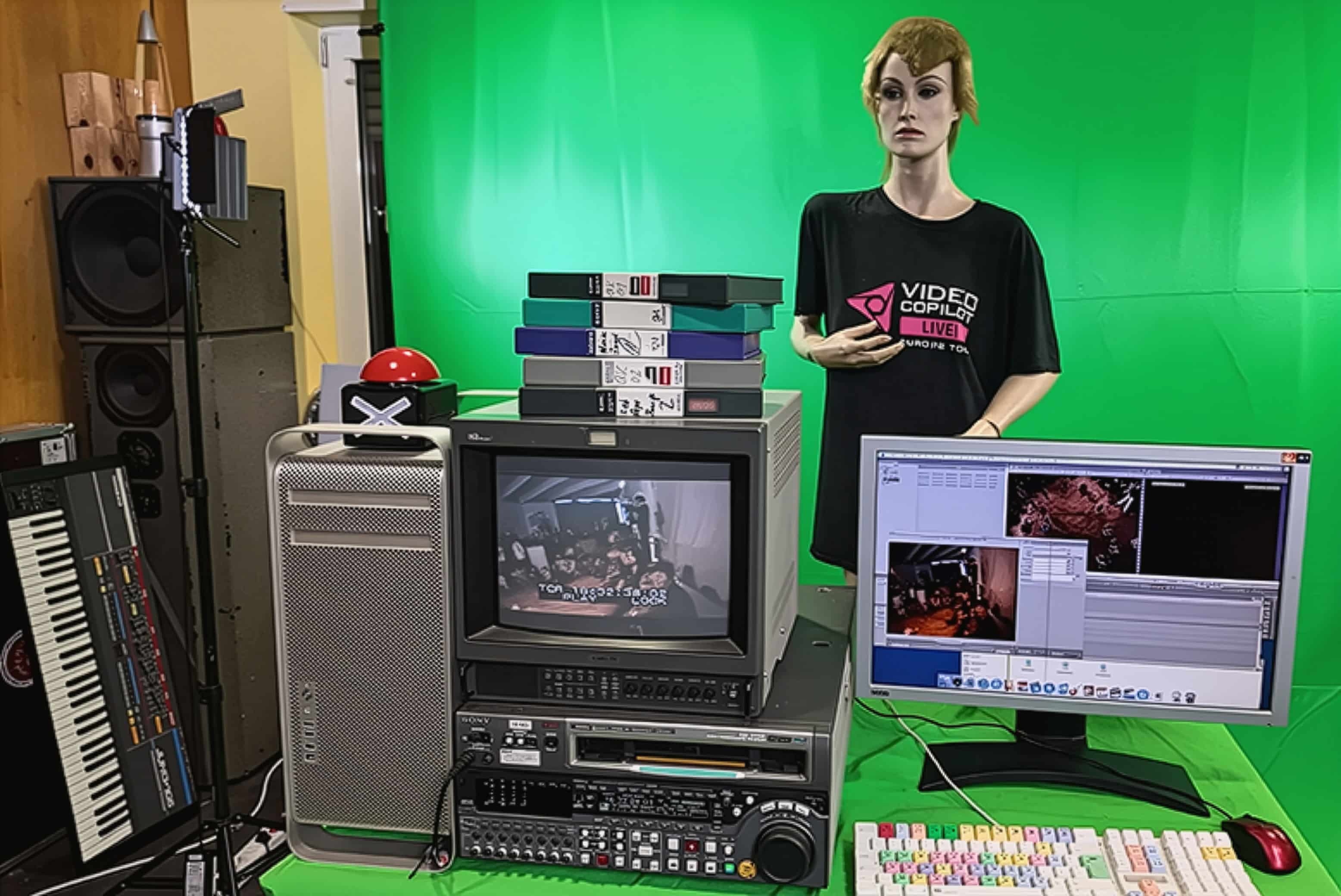 A workspace featuring a mannequin wearing a black shirt with "VIDEO COLLECTION" text. In front, a CRT monitor displays video content, surrounded by VHS tapes. A computer monitor shows editing software. The background is green.