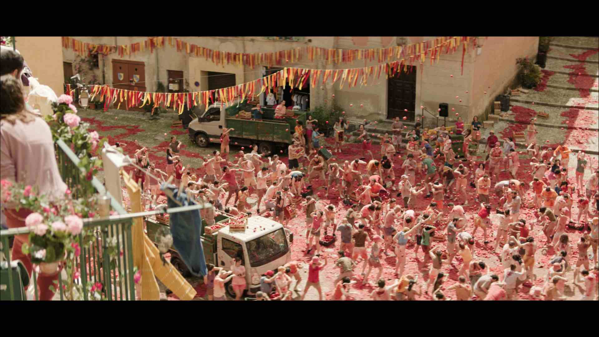 a large crowd of people celebrating in a street covered with red liquid surrounded by colorful banners some individuals are on a balcony observing the festivities a white van is parked nearby digital production A large crowd of people celebrating in a street covered with red liquid, surrounded by colorful banners. Some individuals are on a balcony observing the festivities. A white van is parked nearby.