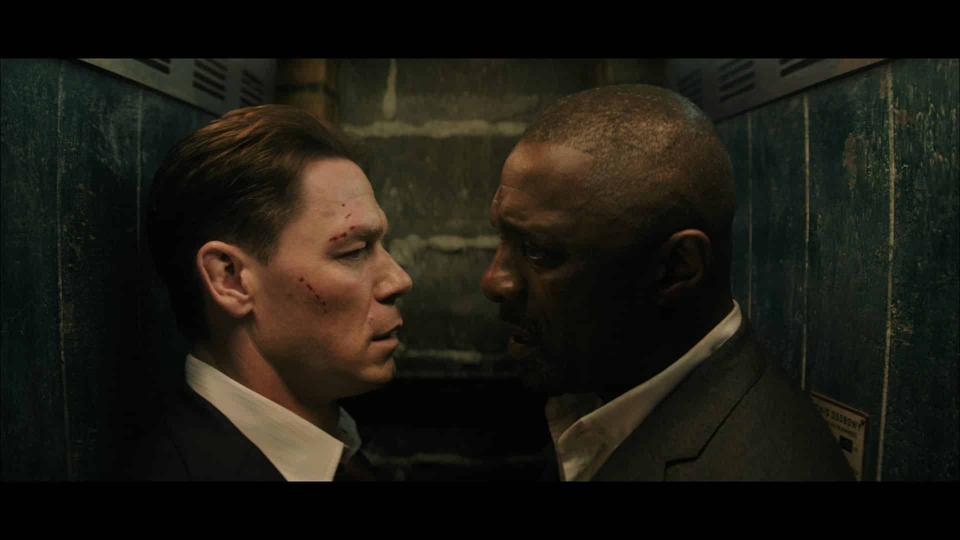 two men facing each other closely in a dimly lit elevator one man has visible bruises on his face and wears a black suit with a white shirt the other man is dressed in a dark suit and has a serious expression digital production Two men facing each other closely in a dimly lit elevator. One man has visible bruises on his face and wears a black suit with a white shirt. The other man is dressed in a dark suit and has a serious expression.