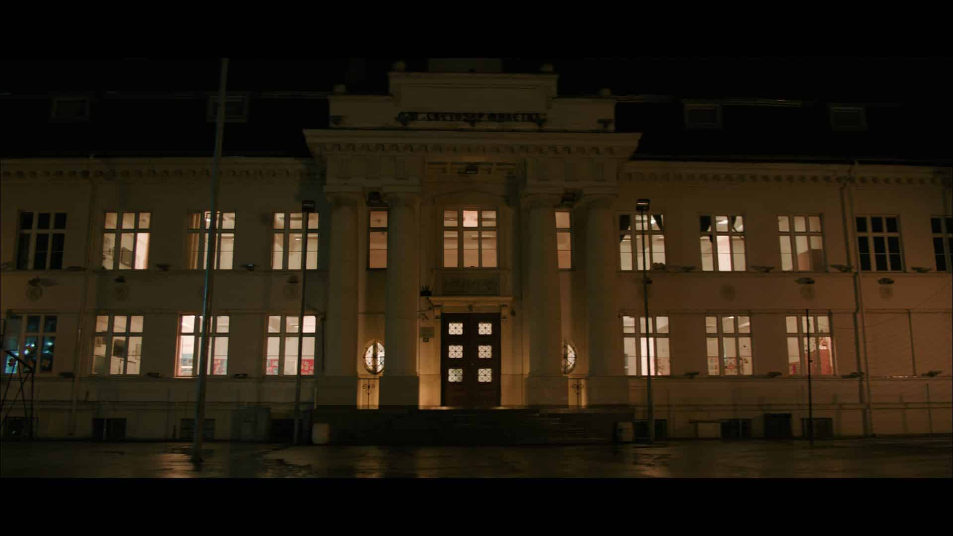 a large building with a prominent entrance illuminated at night the façade features multiple windows and decorative elements street lamps are visible in front of the building digital production A large building with a prominent entrance, illuminated at night. The façade features multiple windows and decorative elements. Street lamps are visible in front of the building.