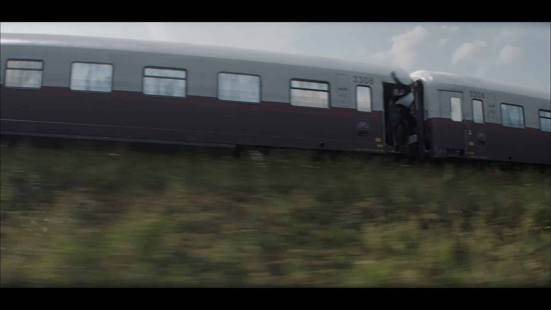 a train car with a door open while the train is in motion a person is seen exiting the train the background shows grass and cloudy skies digital production A train car with a door open while the train is in motion. A person is seen exiting the train. The background shows grass and cloudy skies.