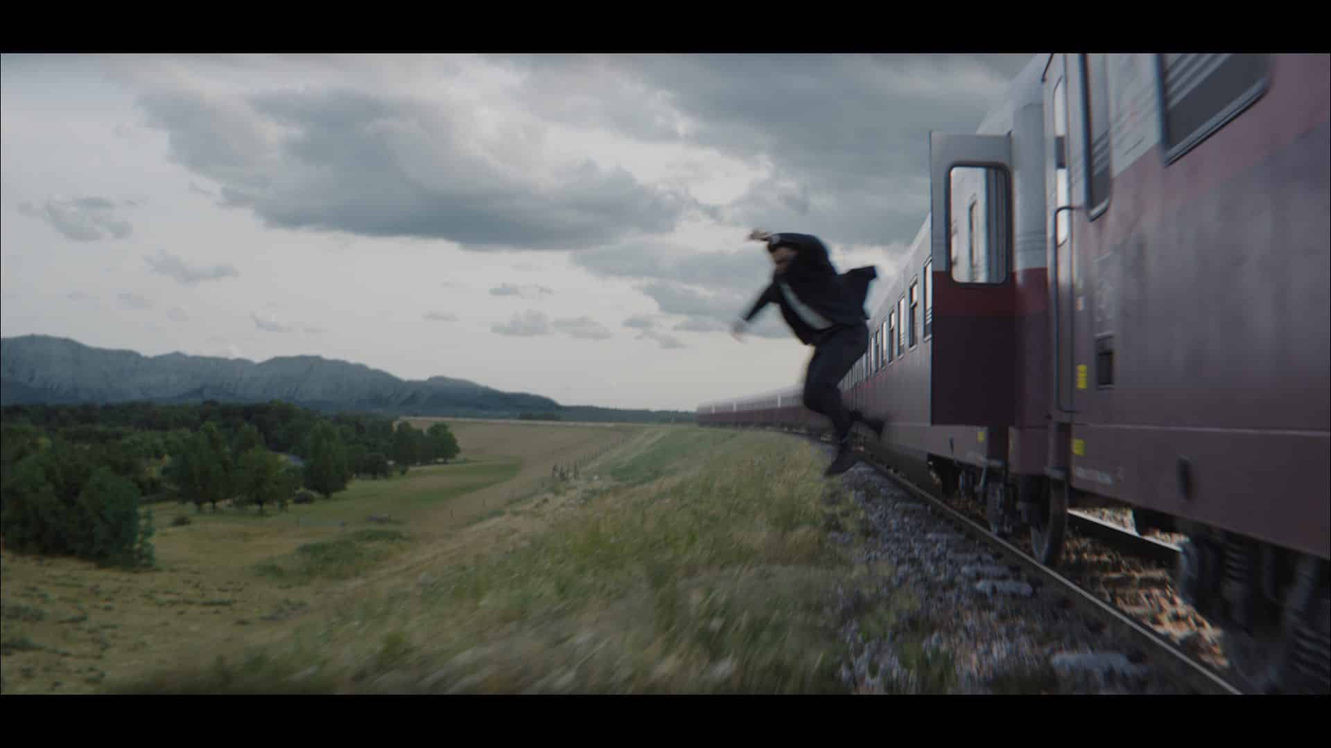 a person jumping off the side of a moving train the train is red and the scene features a green landscape with trees and mountains in the background under a cloudy sky digital production A person jumping off the side of a moving train. The train is red, and the scene features a green landscape with trees and mountains in the background under a cloudy sky.