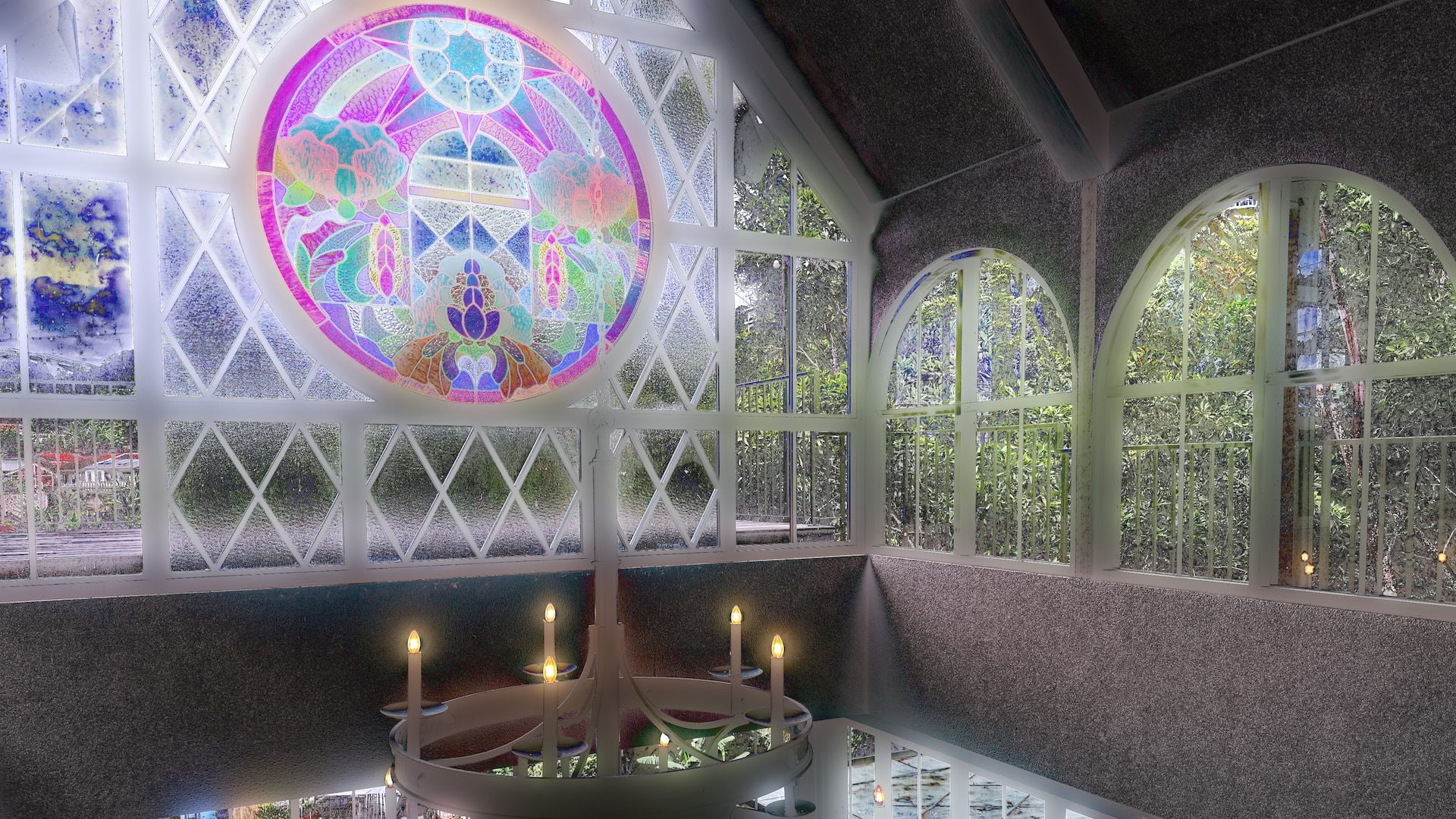 an interior view of a room with large arched windows a colorful stained glass window dominates one wall and a circular table with candles is in the foreground lush greenery can be seen outside digital production An interior view of a room with large arched windows. A colorful stained glass window dominates one wall, and a circular table with candles is in the foreground. Lush greenery can be seen outside.