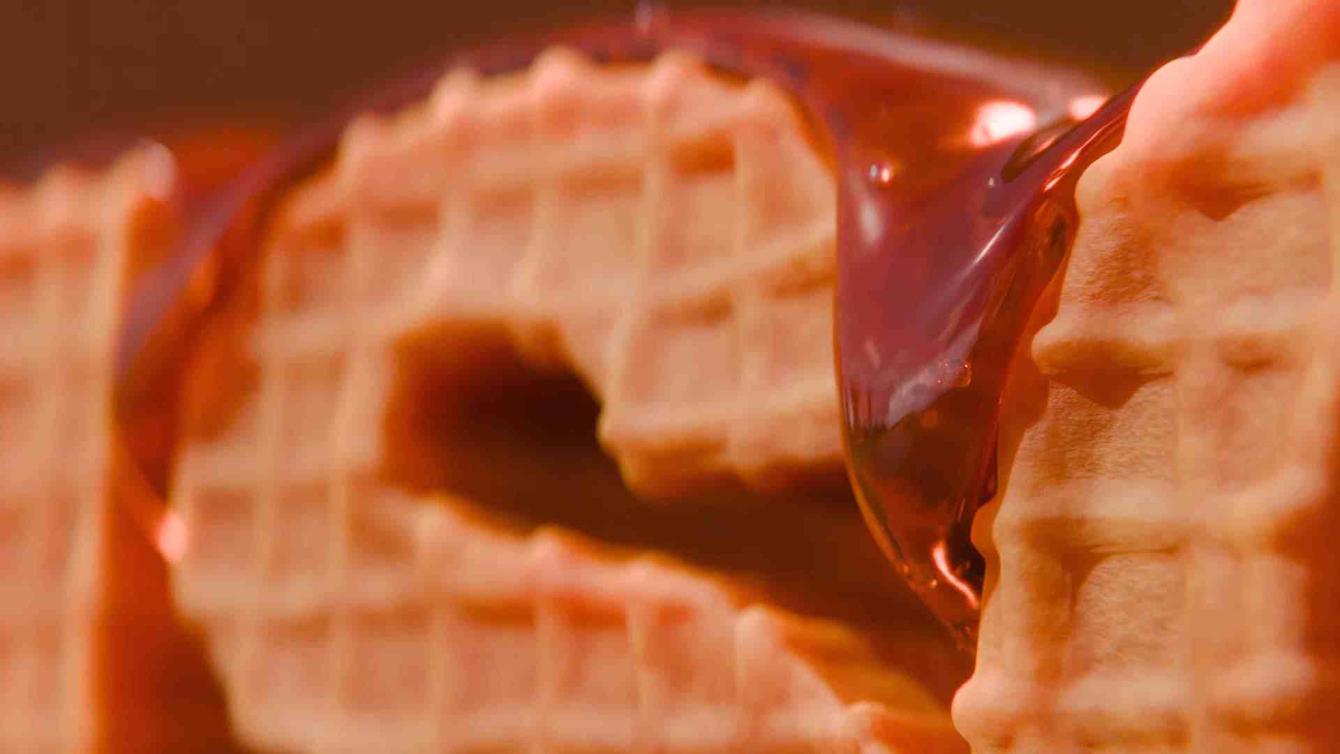 closeup of a waffle with a shiny chocolate coating drizzled over it the waffle has a textured grid pattern and appears slightly broken revealing its inner layers digital production Close-up of a waffle with a shiny chocolate coating drizzled over it. The waffle has a textured grid pattern and appears slightly broken, revealing its inner layers.