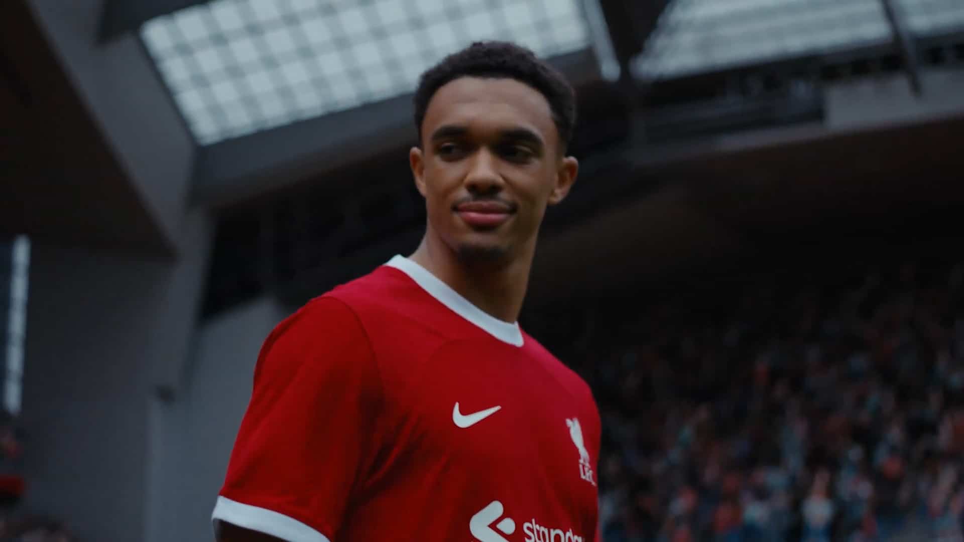 a football player wearing a red liverpool fc jersey stands on the pitch with a stadium filled with fans in the background the player has short curly hair and is looking to the side digital production A football player wearing a red Liverpool FC jersey stands on the pitch with a stadium filled with fans in the background. The player has short curly hair and is looking to the side.