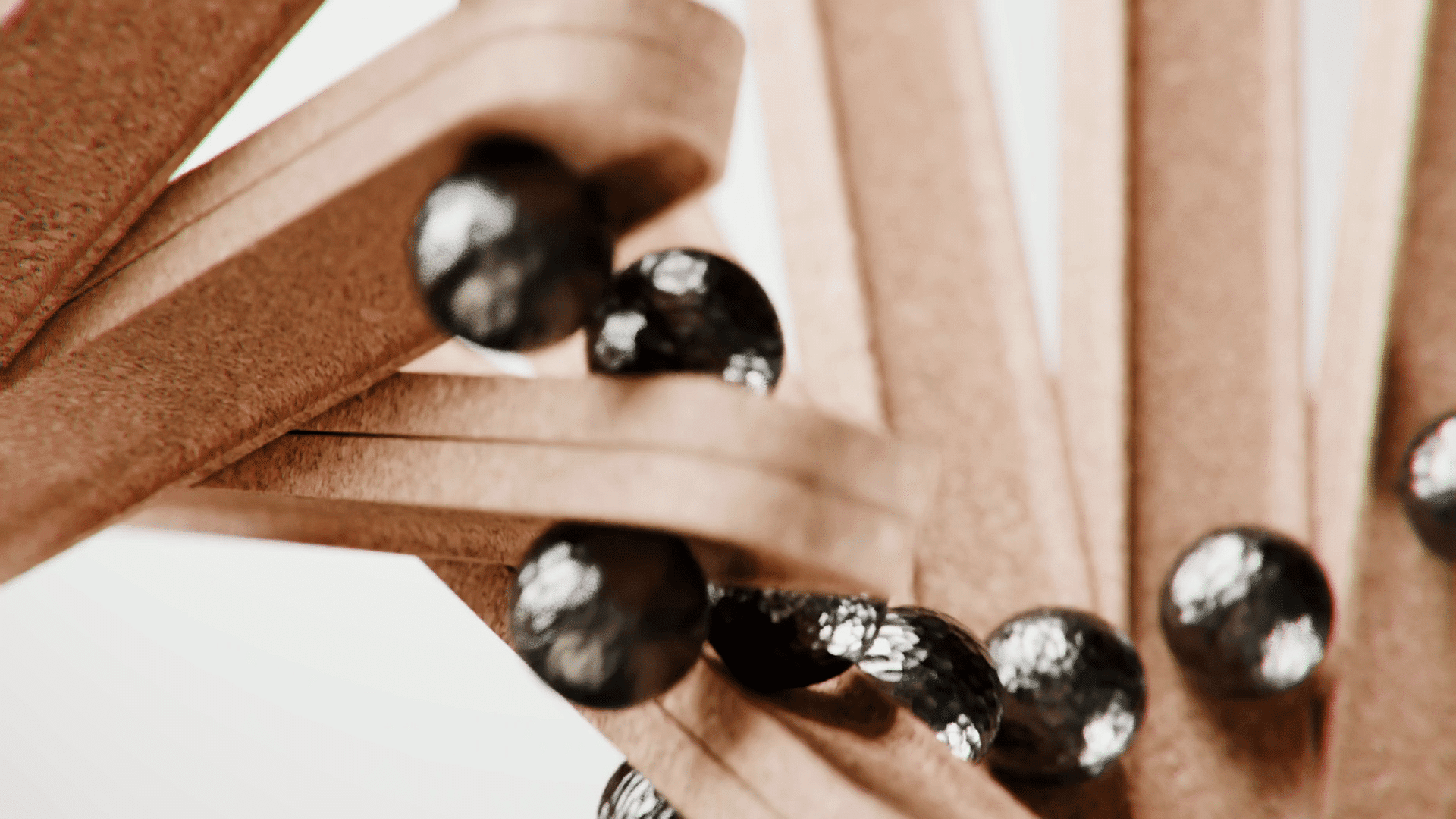 a closeup view of a creative structure made with wooden elements and shiny black balls the wood pieces intertwine elegantly allowing the balls to roll smoothly along the curves set against a light background digital production A close-up view of a creative structure made with wooden elements and shiny black balls. The wood pieces intertwine elegantly, allowing the balls to roll smoothly along the curves, set against a light background.