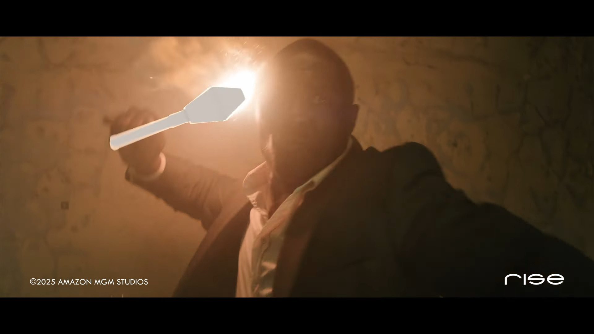 a man in a dark smoky room holding a light source that illuminates his face he is wearing a suit and has an intense expression as if he is in an action scene the background appears distressed and shadowy digital production A man in a dark, smoky room holding a light source that illuminates his face. He is wearing a suit and has an intense expression, as if he is in an action scene. The background appears distressed and shadowy.