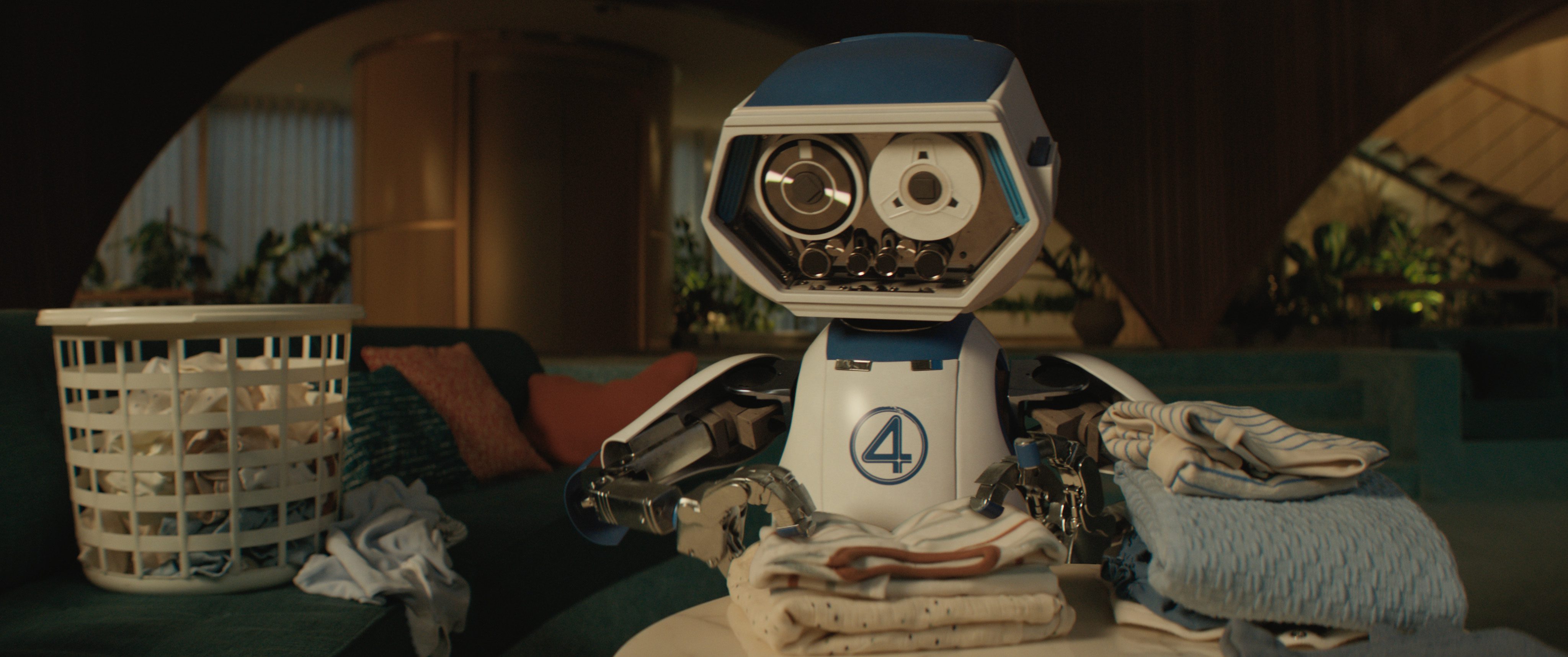 a humanoid robot with a blue head and white body sits on a sofa surrounded by folded laundry and a laundry basket the setting features a cozy living room with soft lighting and modern design elements digital production A humanoid robot with a blue head and white body sits on a sofa, surrounded by folded laundry and a laundry basket. The setting features a cozy living room with soft lighting and modern design elements.
