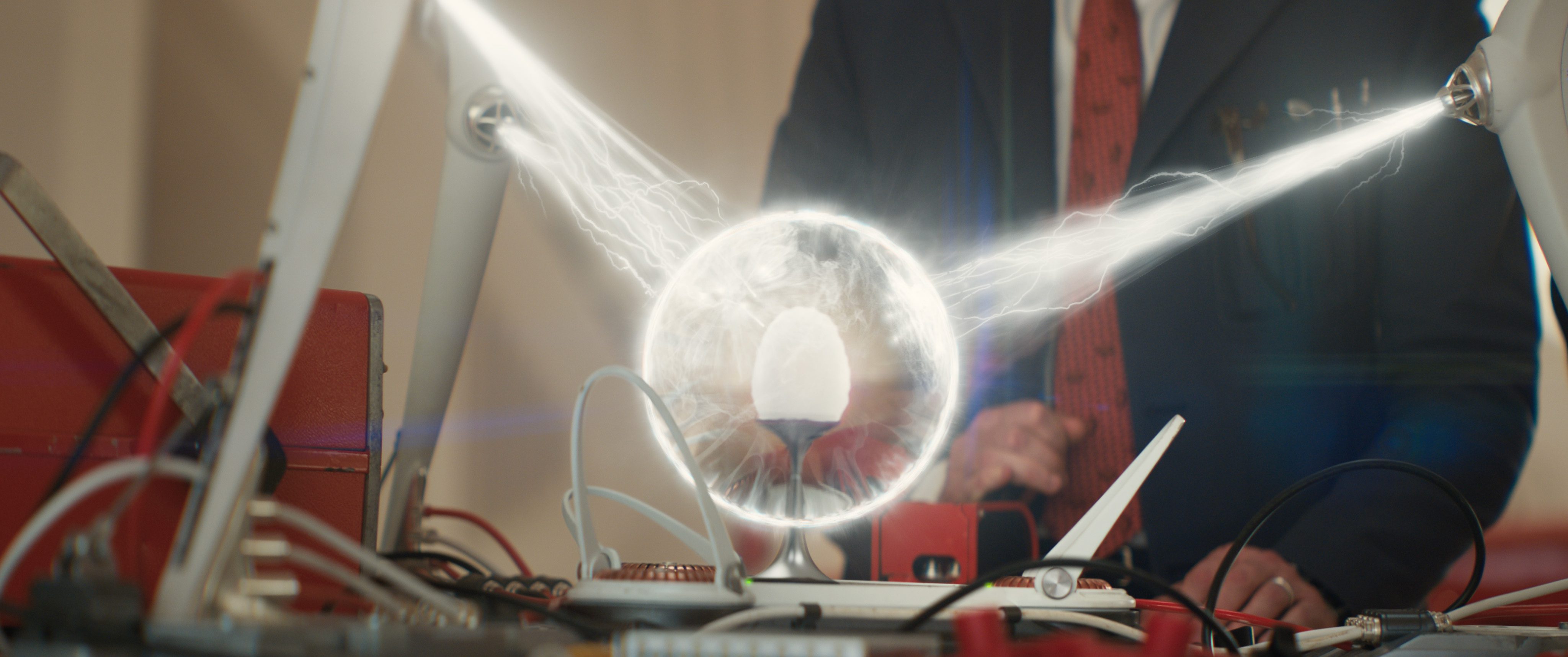 a man in formal attire stands behind a table filled with various scientific equipment in the center a glowing orb emits bright beams of light creating an energetic atmosphere wires and instruments are scattered around the setup digital production A man in formal attire stands behind a table filled with various scientific equipment. In the center, a glowing orb emits bright beams of light, creating an energetic atmosphere. Wires and instruments are scattered around the setup.