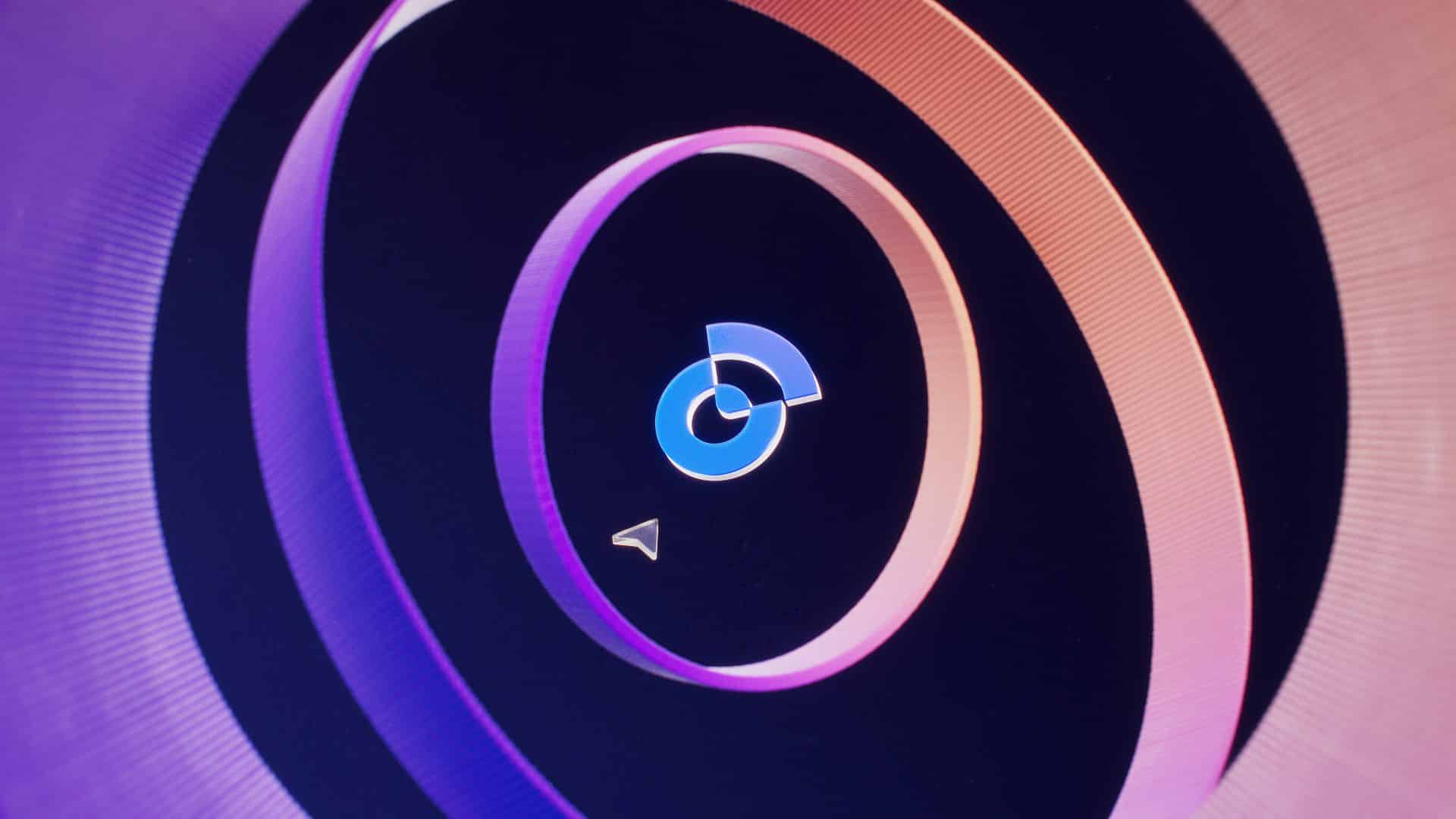 a closeup view of a digital interface showcasing concentric circles in shades of black purple and orange with a blue circular icon at the center a small triangular pointer is positioned below the icon digital production A close-up view of a digital interface showcasing concentric circles in shades of black, purple, and orange, with a blue circular icon at the center. A small triangular pointer is positioned below the icon.